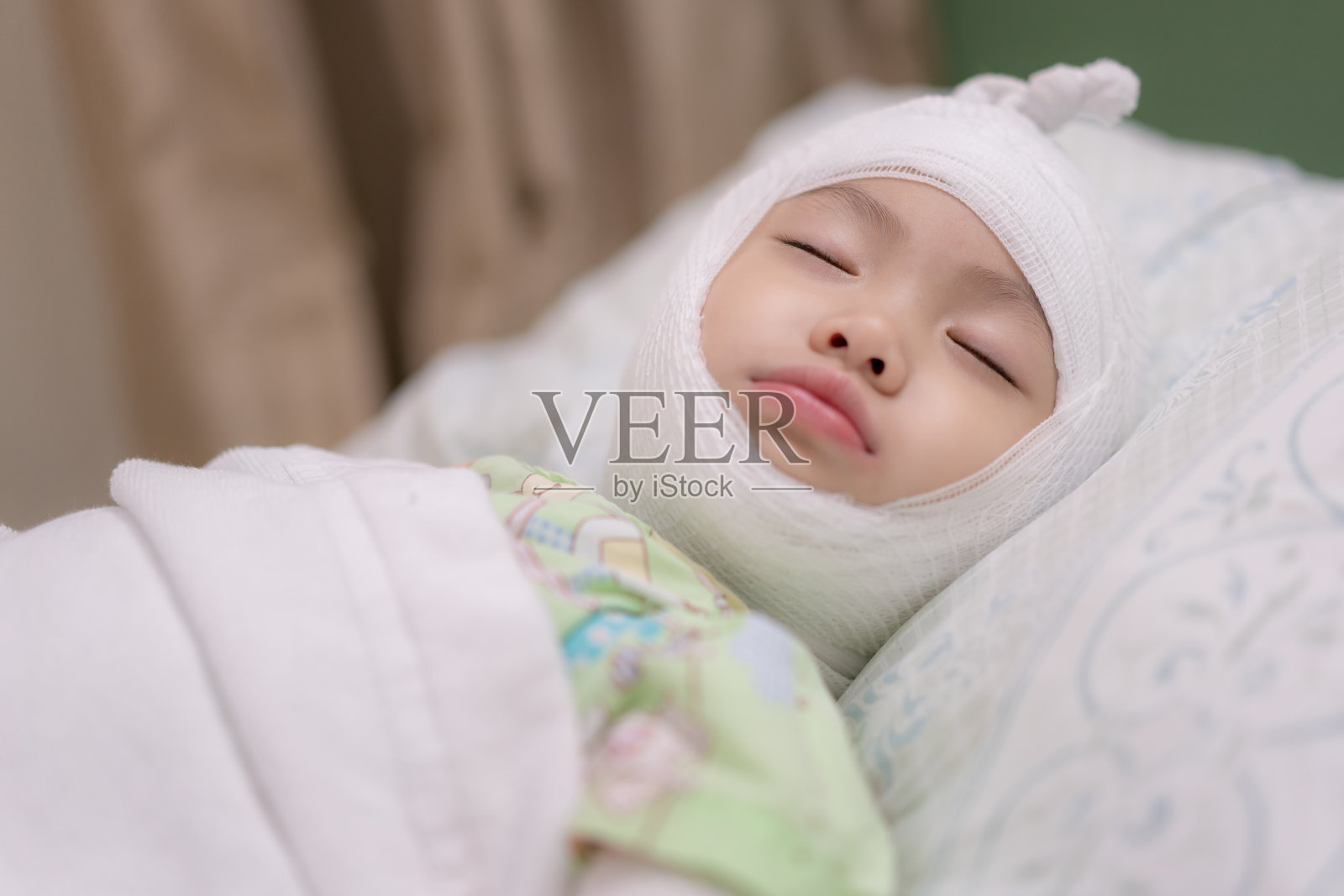 一个亚洲小女孩躺在医院的病床上，头部缠着绷带。女婴受伤头痛。照片摄影图片