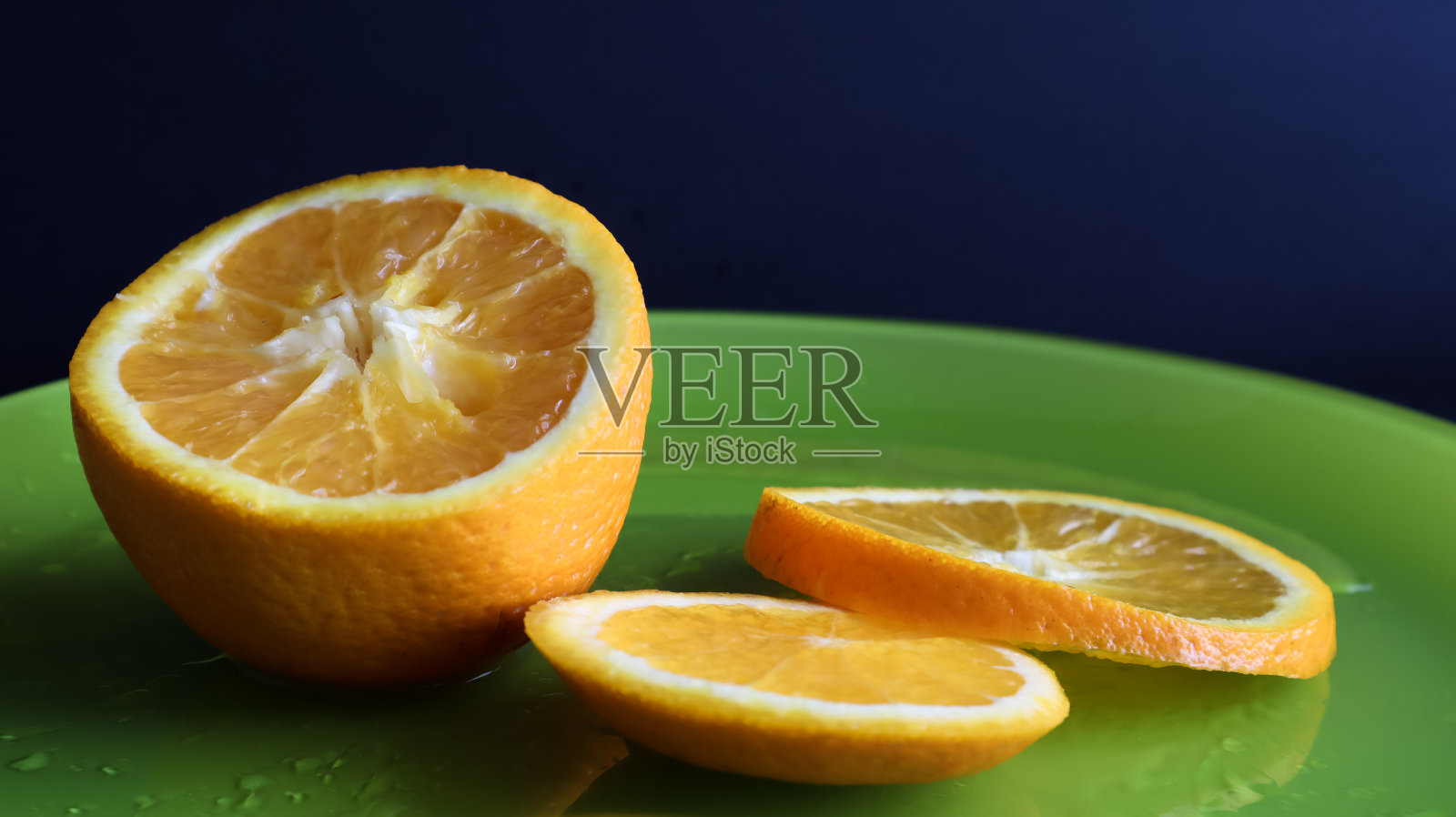 在一张黑色背景的桌子上，把半个橙子切成薄片，放在一个有水滴的绿色玻璃盘子里。果实多嵌套，多籽，有厚厚的两层果皮照片摄影图片