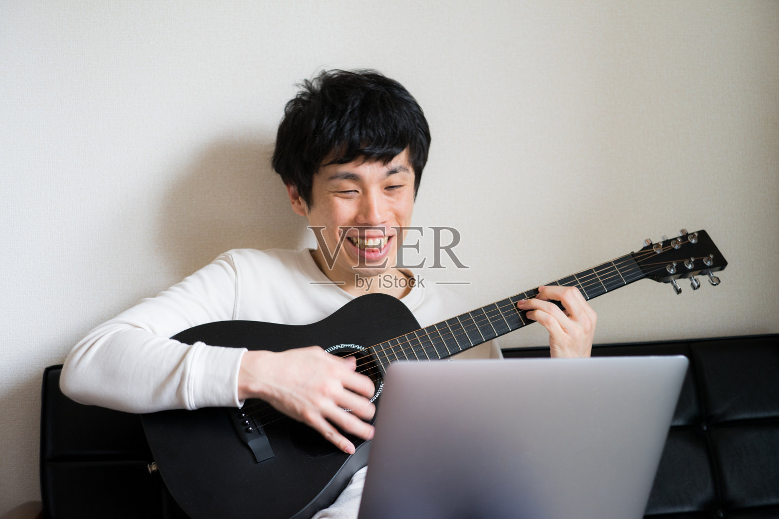 年轻人坐在沙发上，在家里弹吉他。照片摄影图片