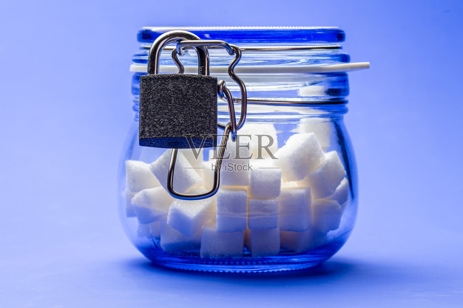 白糖块放在一个透明的玻璃罐中，瓶盖锁上，以蓝色为背景。适当营养的概念。照片摄影图片