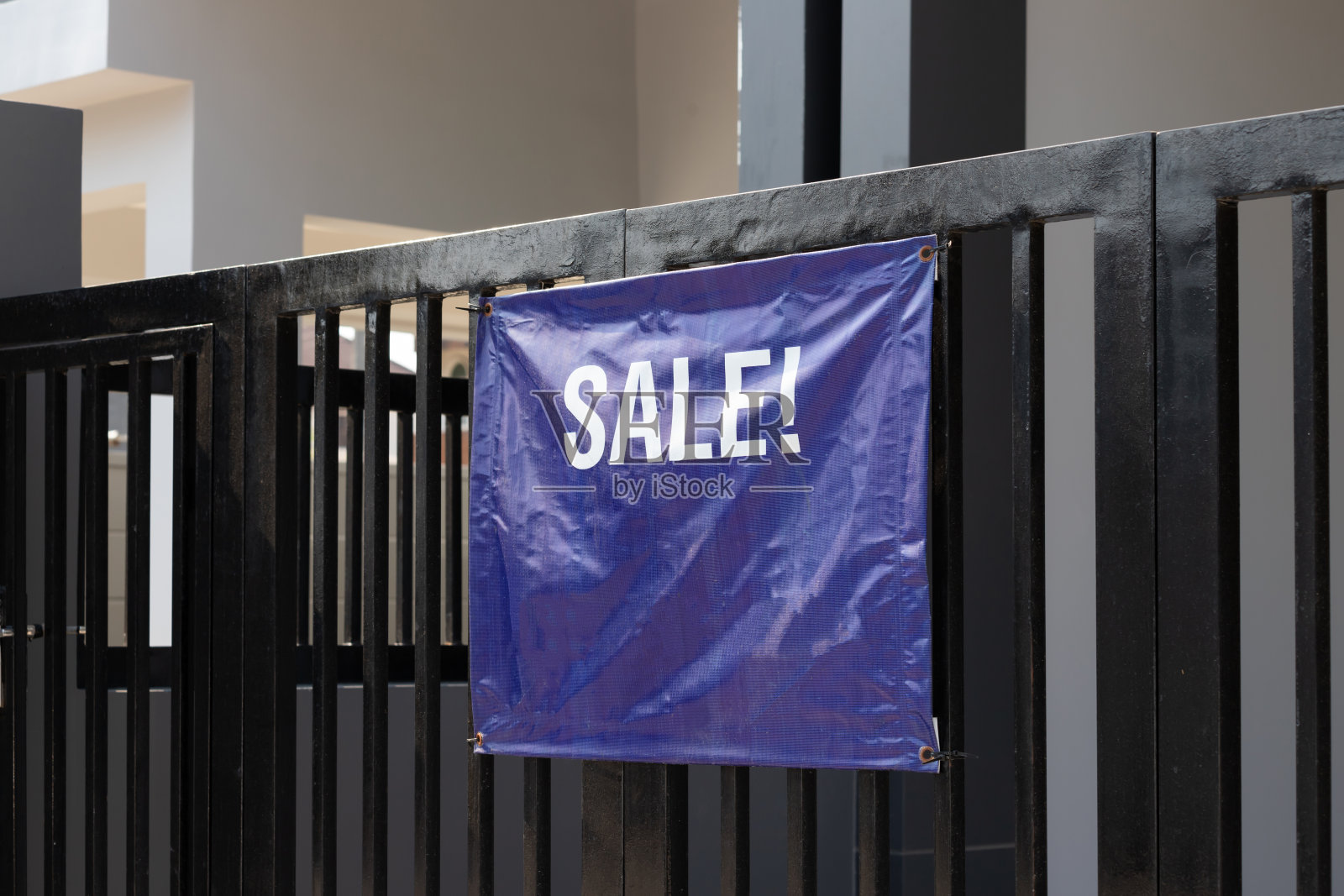 黑色金属栅栏上的蓝色帆布。出售告示。概念:出售房屋或居民。照片摄影图片