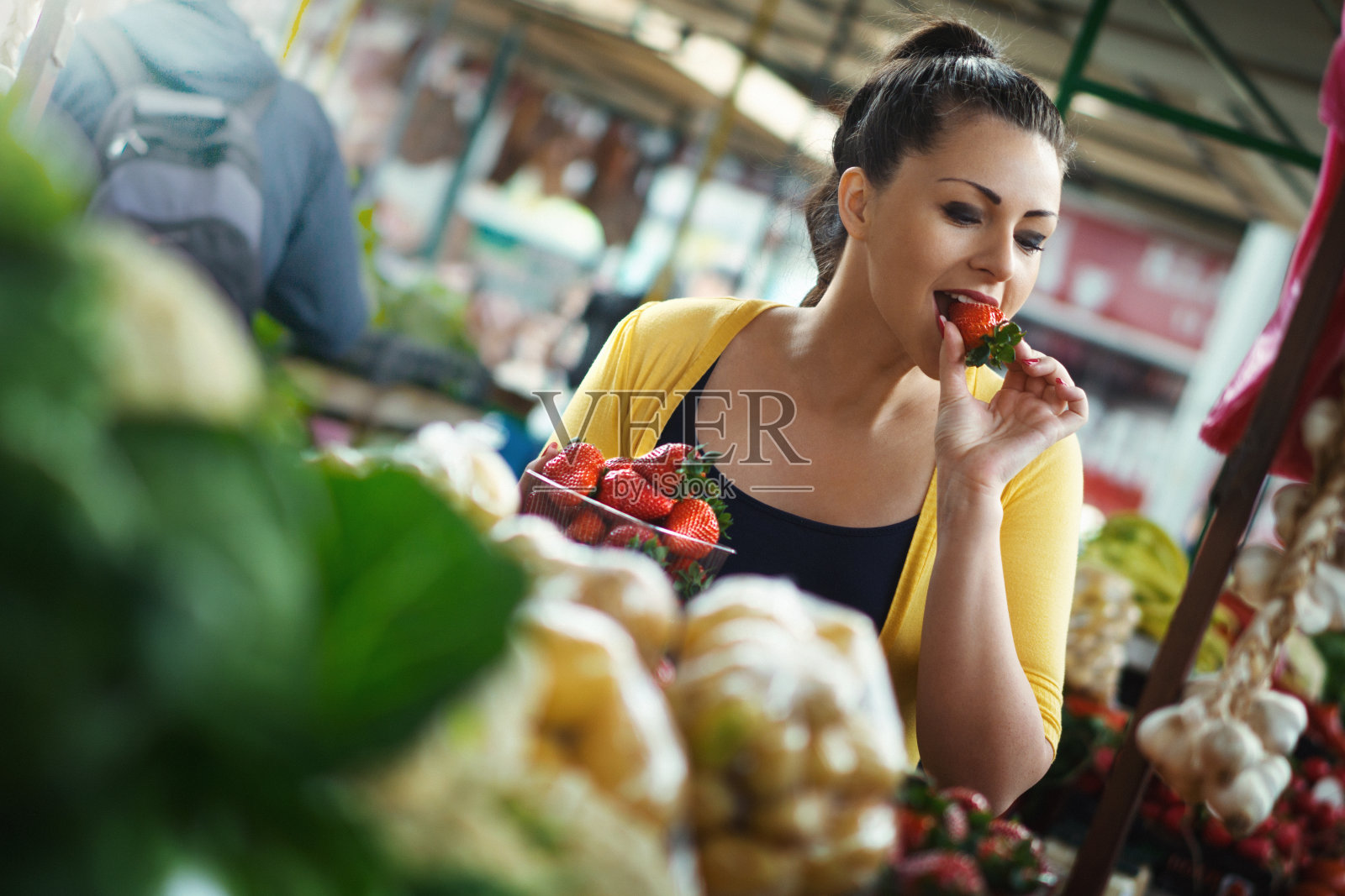 年轻女子在食品市场品尝草莓。照片摄影图片
