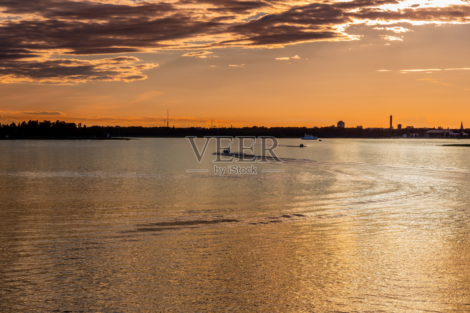 美丽的金色日落在瑞典的凡恩湖与城市和天空地平线。轮船和小船。照片摄影图片