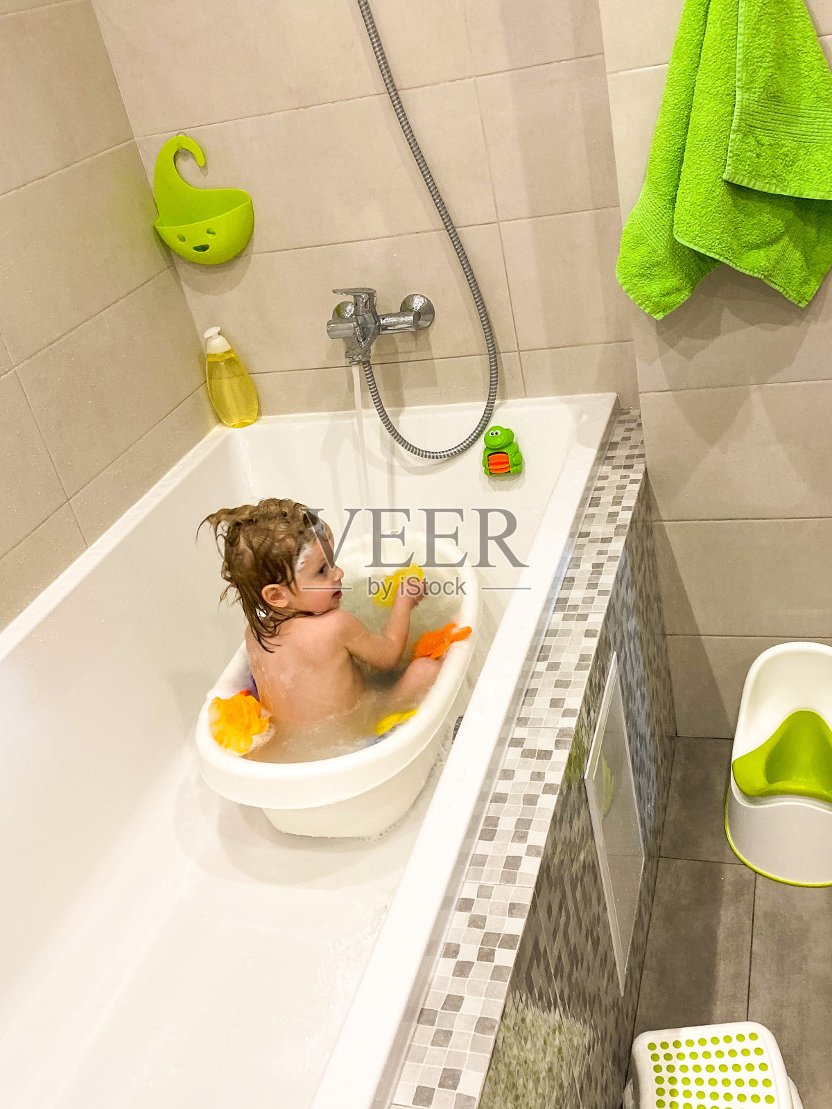 皮肤白皙的小孩/婴儿在浴缸里用肥皂水和玩具洗澡。照片摄影图片