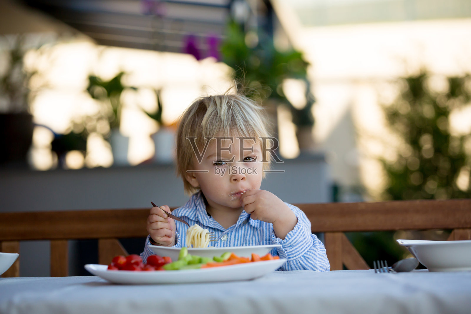 可爱的孩子，蹒跚学步的金发男孩，在花园里吃意大利面照片摄影图片