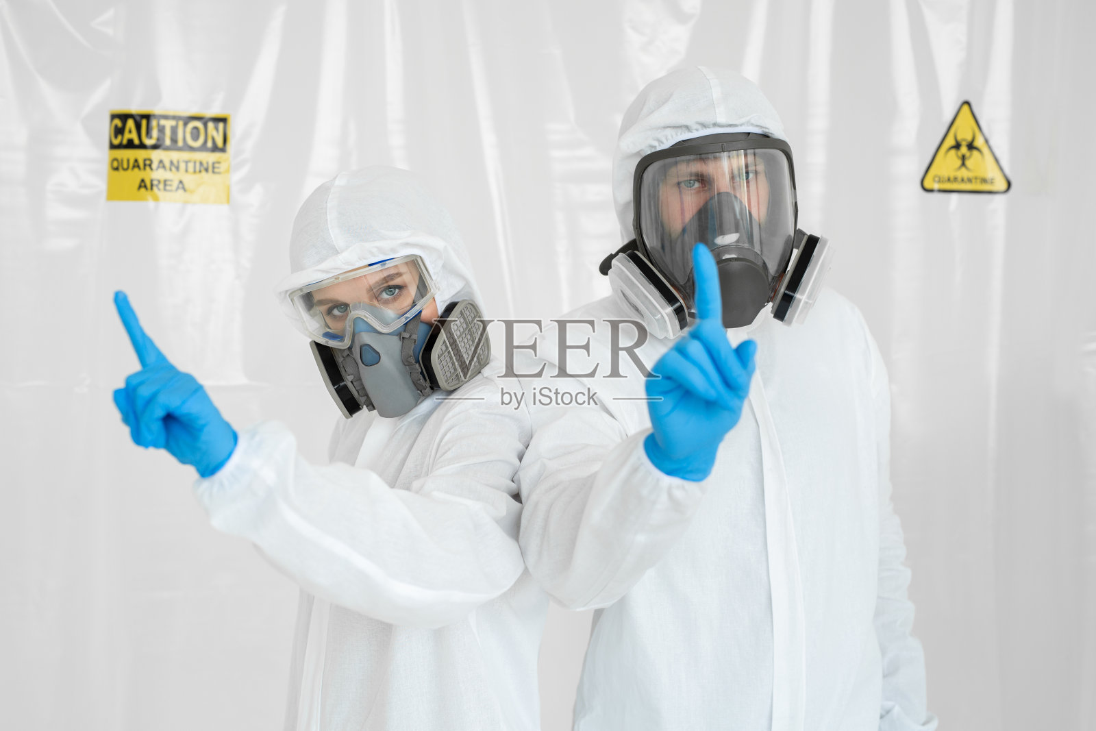 两名医生，一男一女穿着防护服，戴着呼吸器，他们用手表示注意。冠状病毒疫情的概念。新型冠状病毒肺炎照片摄影图片