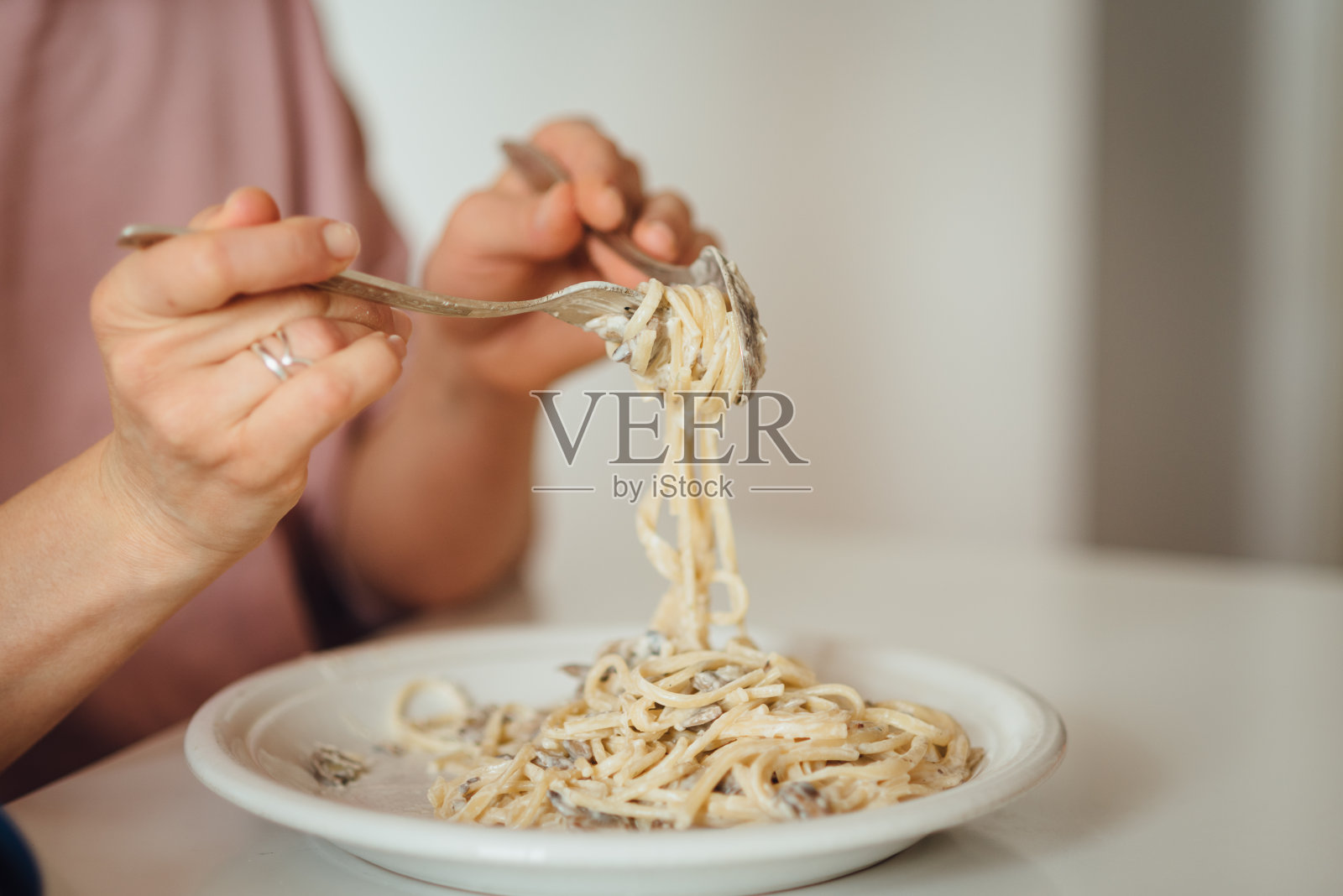 年轻女子吃蘑菇意大利面。特写的意大利面用勺子把它绕在叉子上照片摄影图片