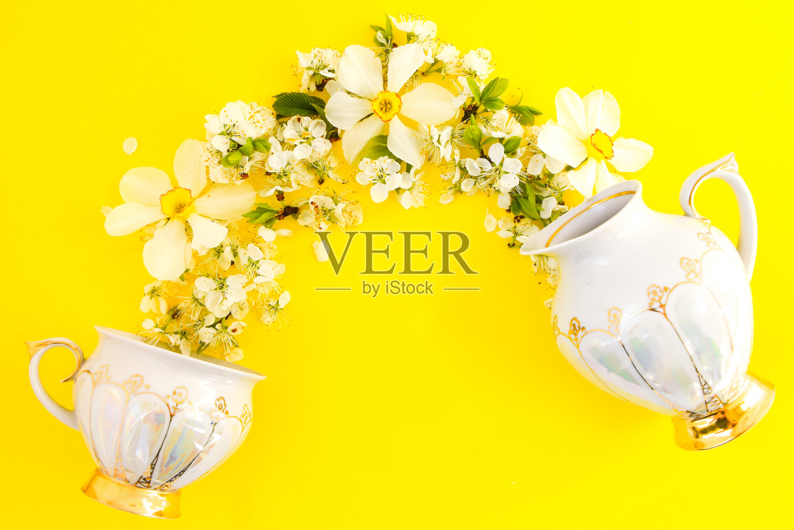 茶壶和茶杯的创意布局，以杏花或樱花为背景的黄色。春天的时间照片摄影图片