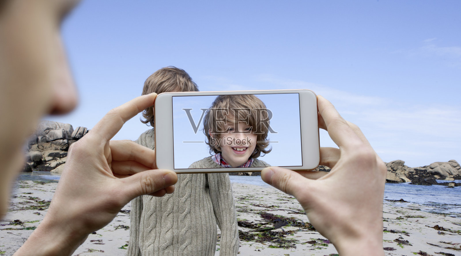 一个年轻人正在用手机拍一个男孩在海滩上的度假照片照片摄影图片