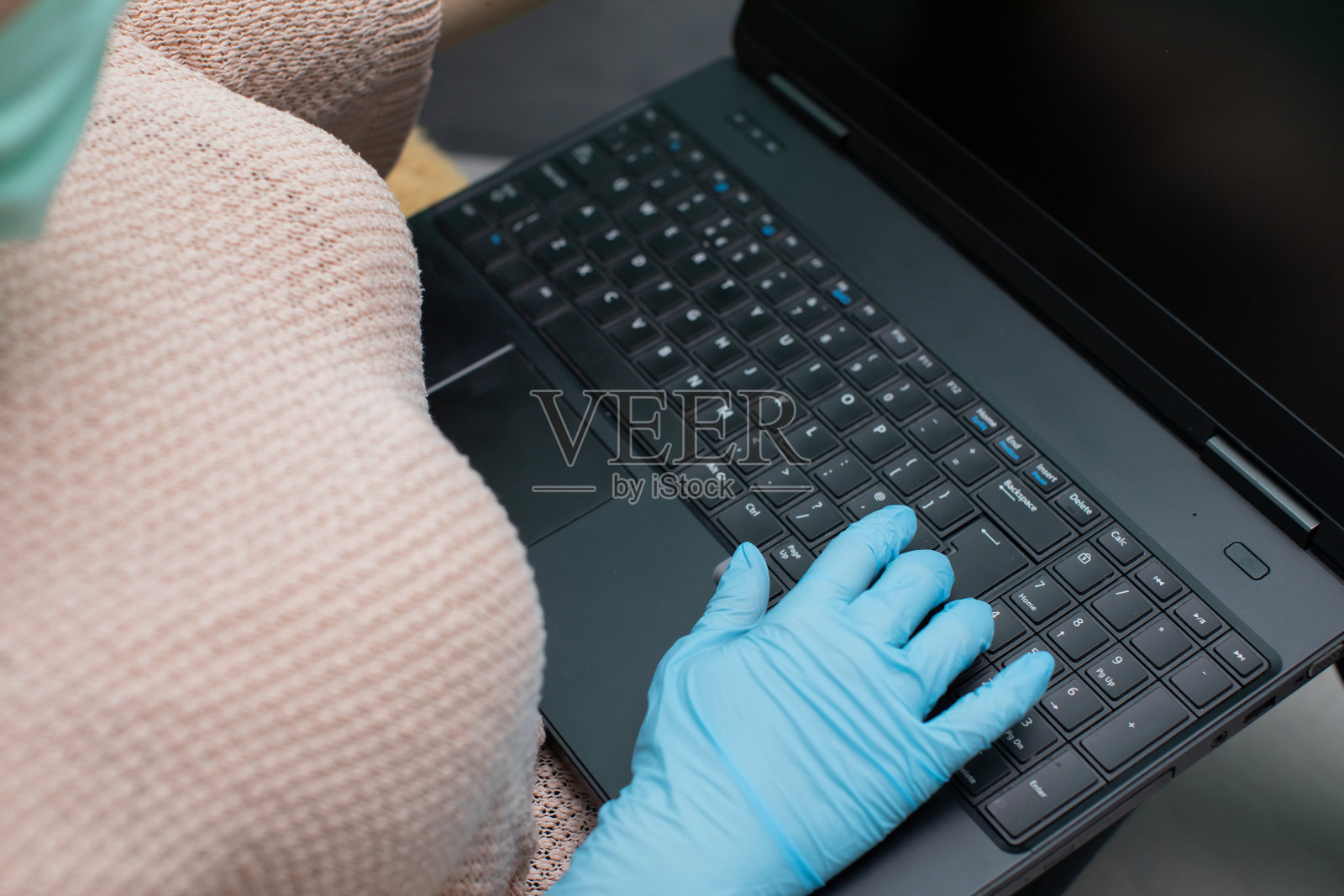 一个戴着橡胶手套的青少年为了安全使用的笔记本电脑键盘。照片摄影图片