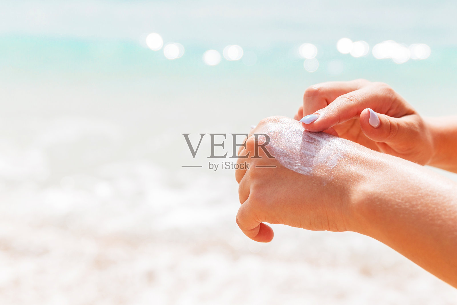 一个穿着泳衣的女人正在用她的手指在大海的背景上涂防晒霜照片摄影图片