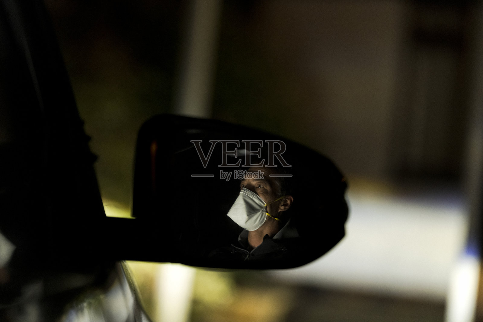 戴着面具的人在晚上开车时，侧面的镜子映出他的身影照片摄影图片