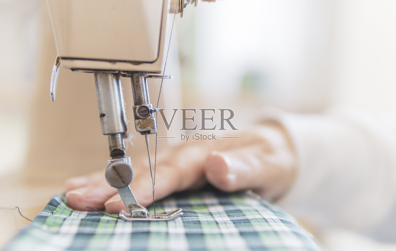 缝纫过程的特写-女性的手在专业机器上缝制织物-在家里缝制的老年妇女-模糊的背景照片摄影图片