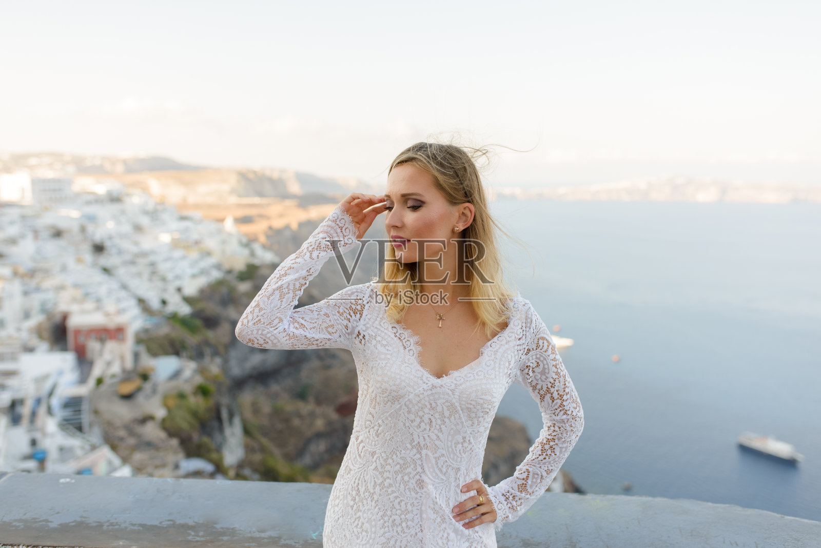 美丽的新娘身穿白色婚纱，在圣托里尼的Thira市的背景下摆姿势。照片摄影图片