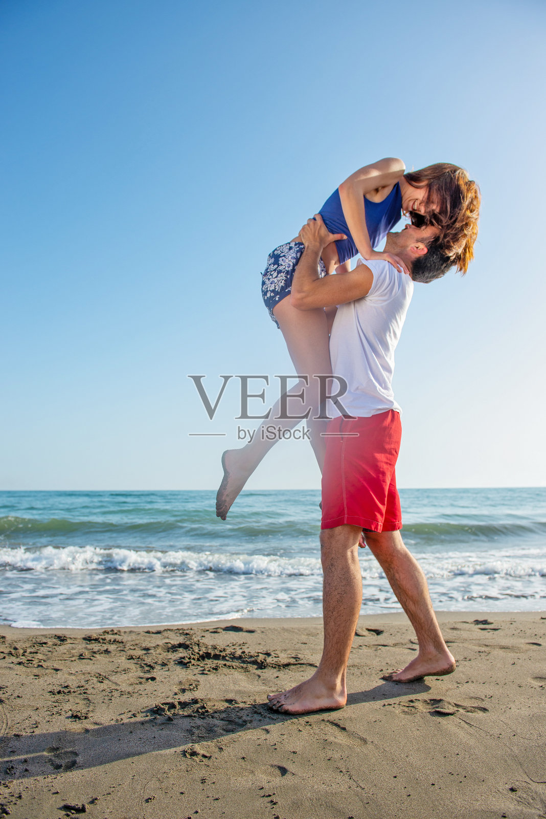 快乐的年轻夫妇在阳光明媚的一天在海滩玩照片摄影图片