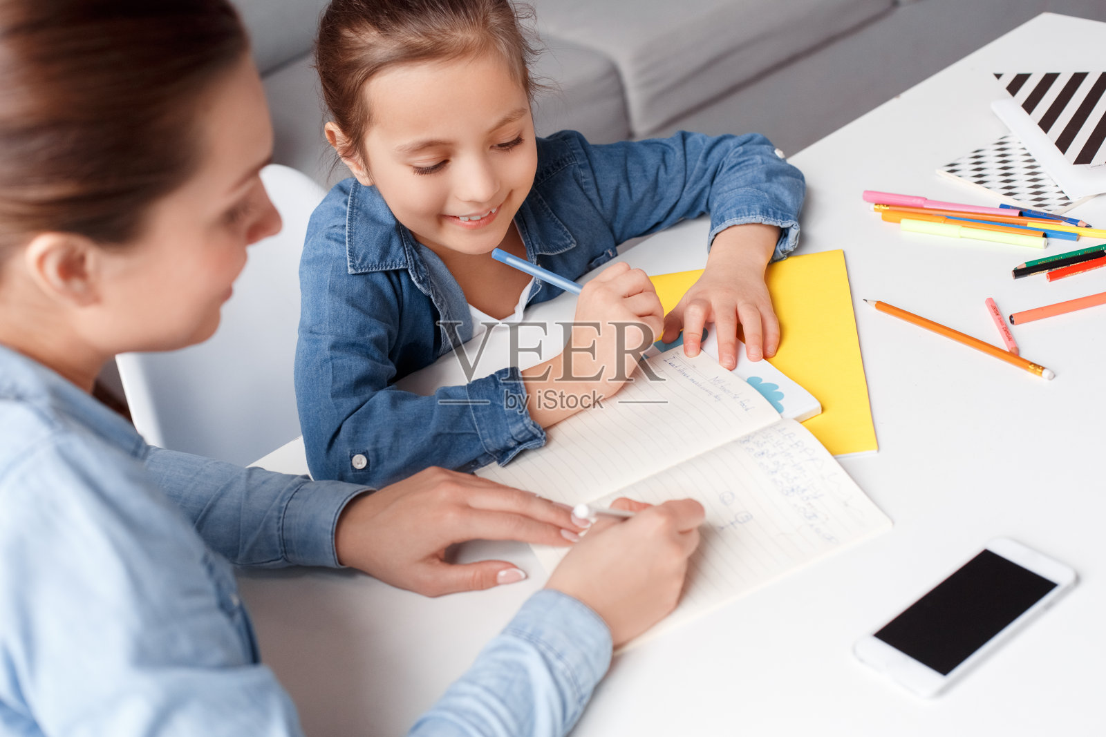 俯视图水平生活方式家庭概念。快乐的妈妈和女儿一起做作业。微笑写，用钢笔画在笔记本上。周末放学后轻松有趣的学习。酷女孩火车照片摄影图片