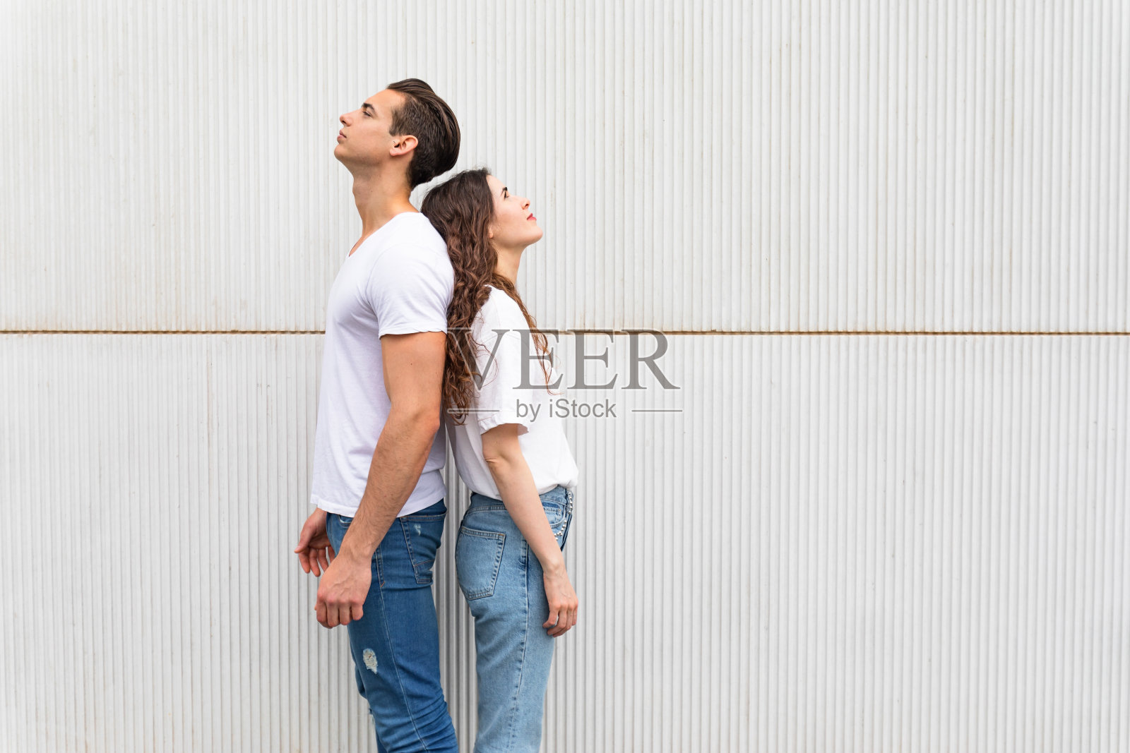 一对年轻夫妇背靠背地站在白色的城市墙壁上照片摄影图片