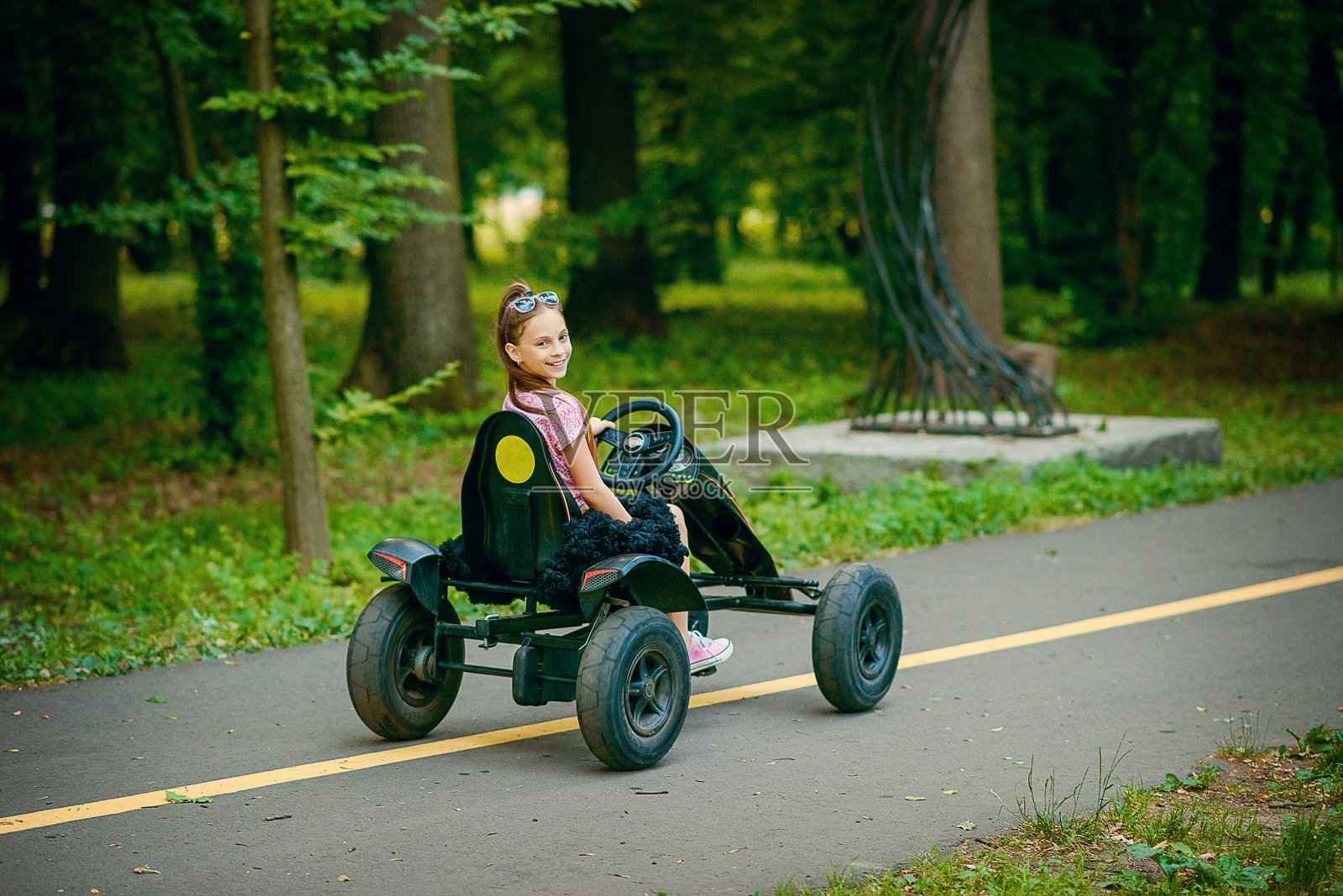 一个漂亮的小女孩穿着蓬松的短裙，拖着一条长长的尾巴，在公园里开着一辆小汽车照片摄影图片