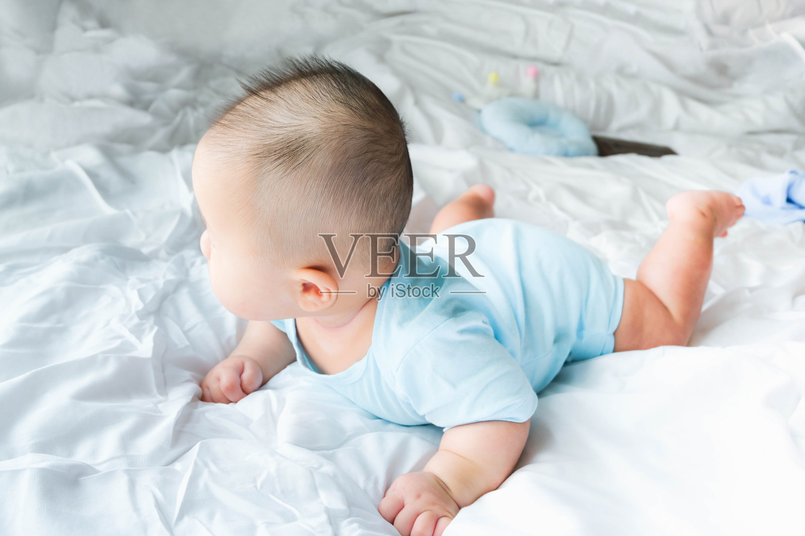 一个刚出生的亚洲可爱男婴穿着蓝色婴儿紧身衣在床上爬行，可爱的胖宝宝5个月大享受和快乐，柔软的选择性焦点照片摄影图片