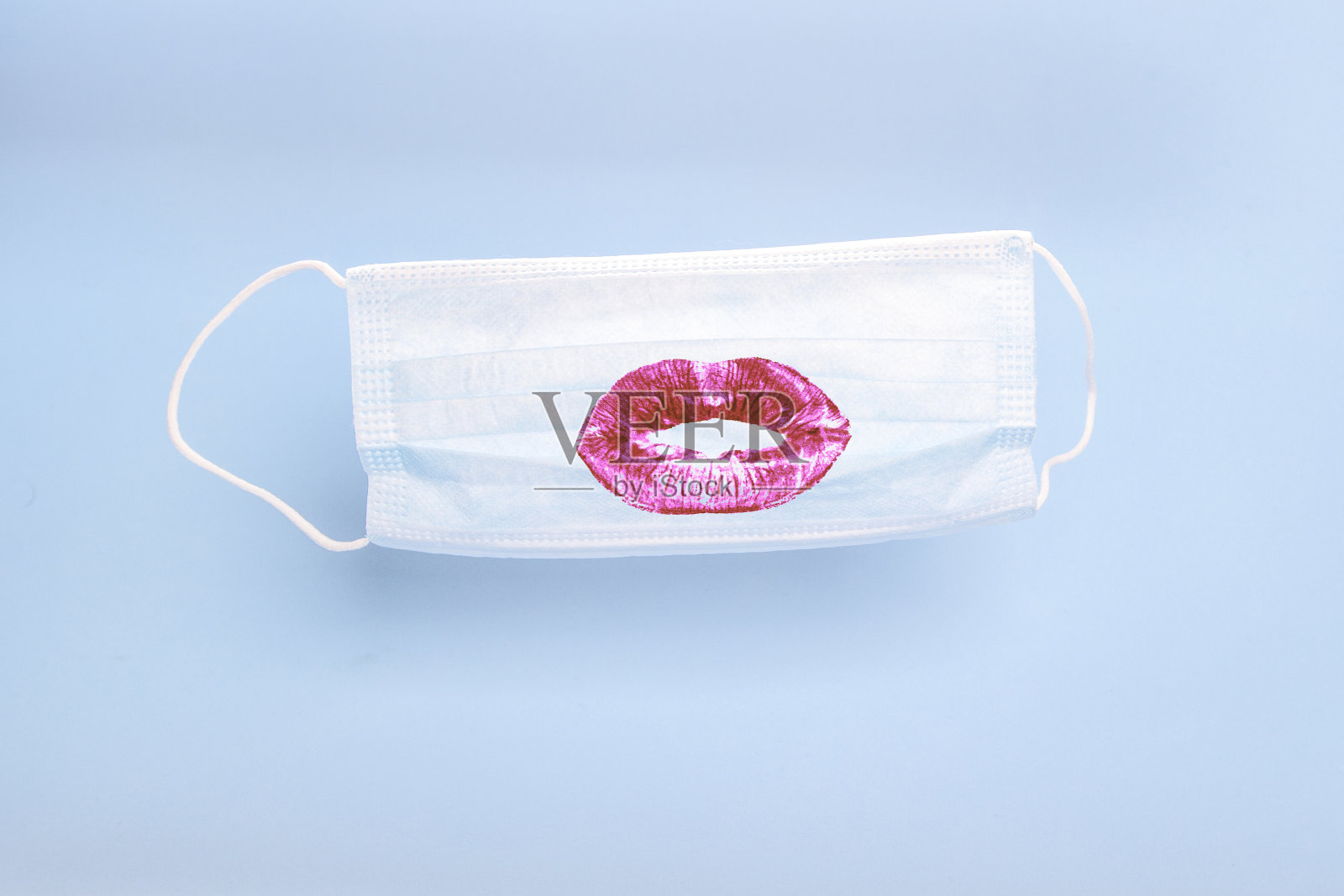 医用口罩与打印的女性口红亲吻嘴唇上的蓝色背景。在冠状病毒(covid - 19)、感冒和病毒性流感流行期间对人口的预防和保护照片摄影图片