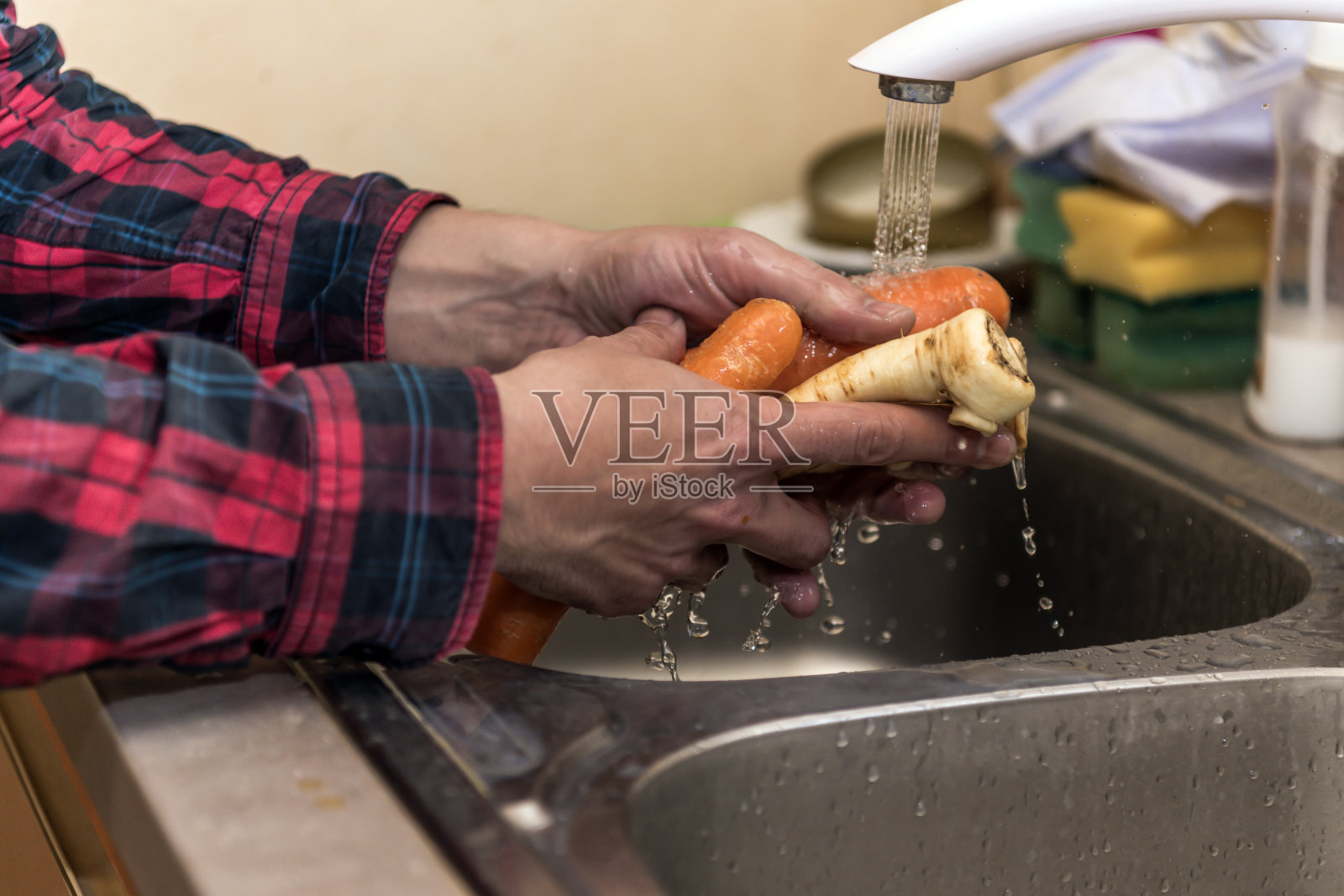 一名男子正在清洗胡萝卜和防风草，准备健康新鲜的早餐。照片摄影图片