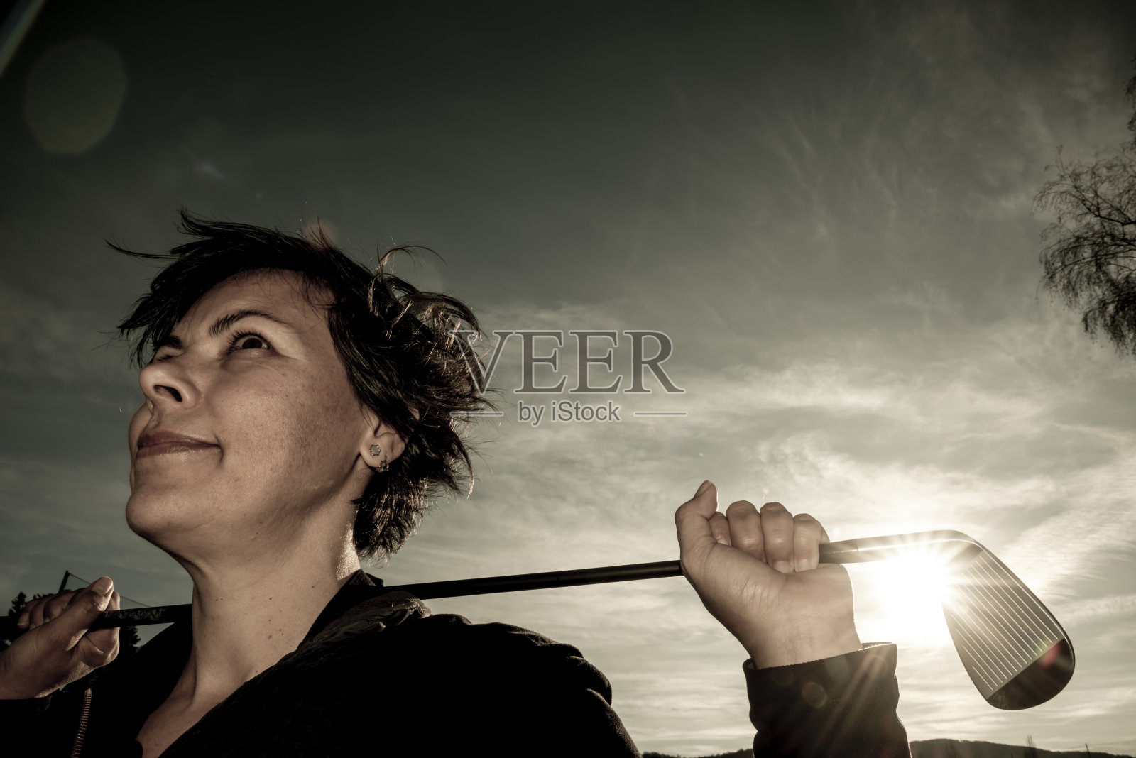 高尔夫球手倚着她的高尔夫球棒在她的肩膀与阳光照片摄影图片