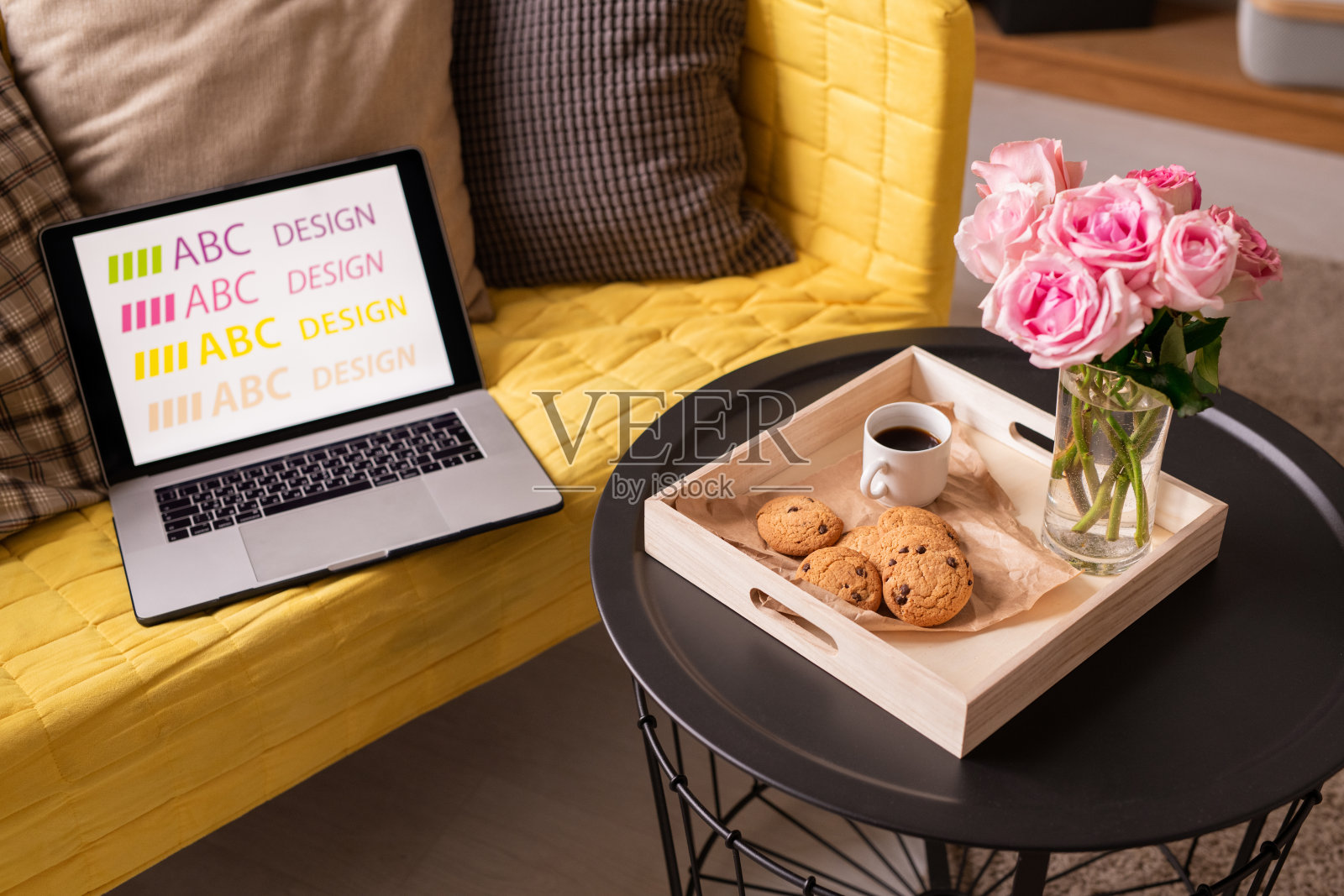 沙发上放着笔记本电脑和靠垫，旁边的小桌子放着鲜花、饮料和饼干照片摄影图片