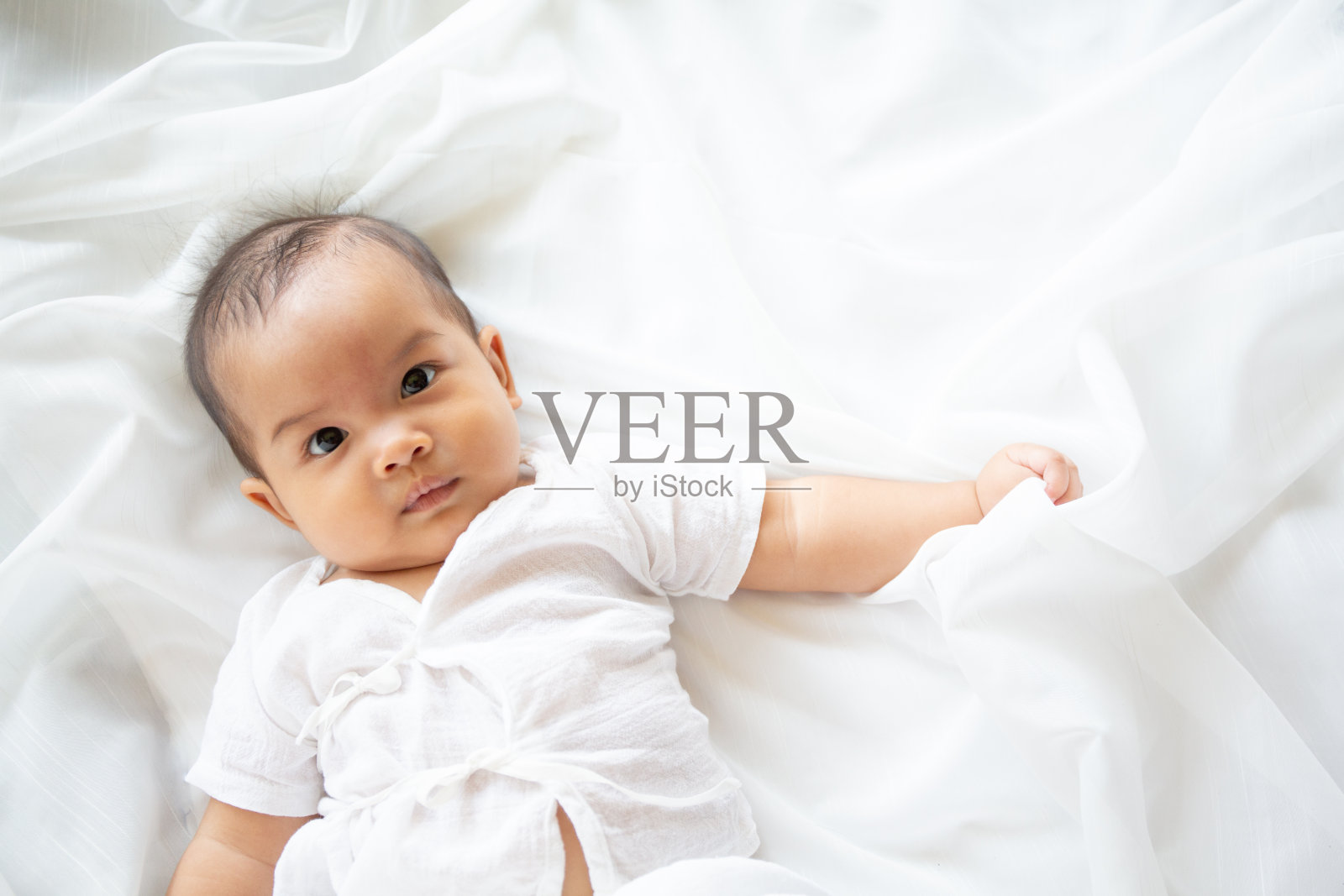 可爱的新生女婴裹着白色的毯子躺在育婴床上。可爱的新生儿，小男孩的眼睛看着人们的家庭，新的童年，婴儿柔软的皮肤肖像概念。黄疸综合症生活医院。照片摄影图片