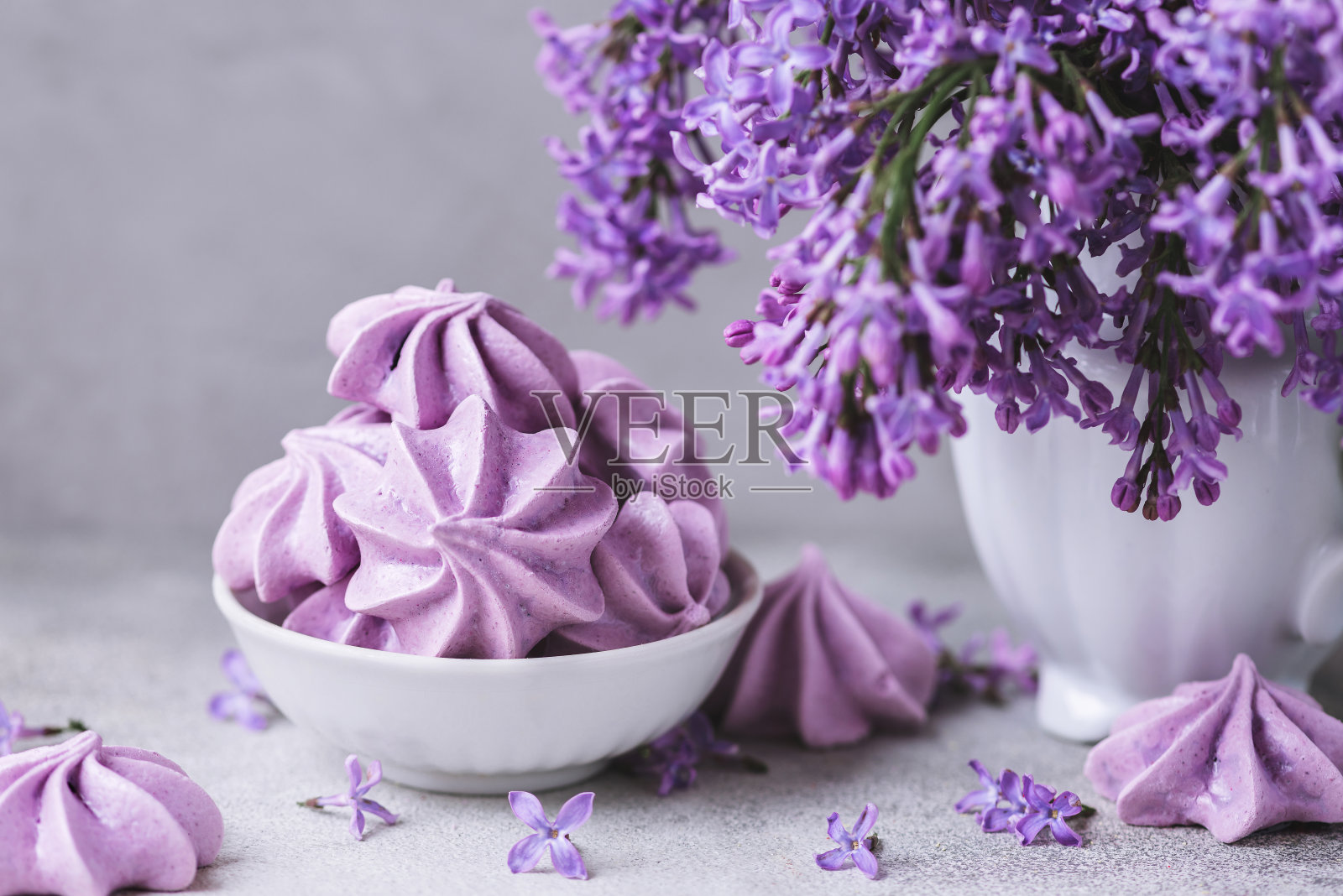 混凝土背景上的花瓶里有紫色的蛋白酥饼和丁香花。复古或instagram色调。静物画照片摄影图片