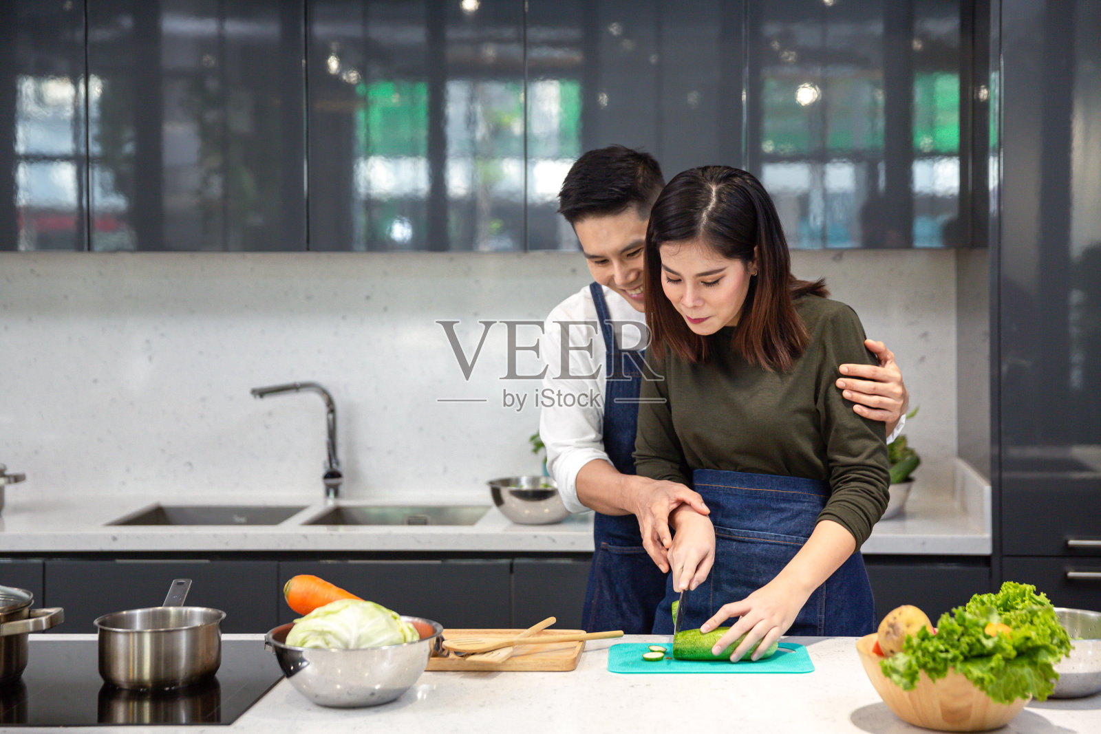 年轻夫妇正在厨房帮忙切蔬菜。一对亚洲夫妇在厨房一起做饭。照片摄影图片