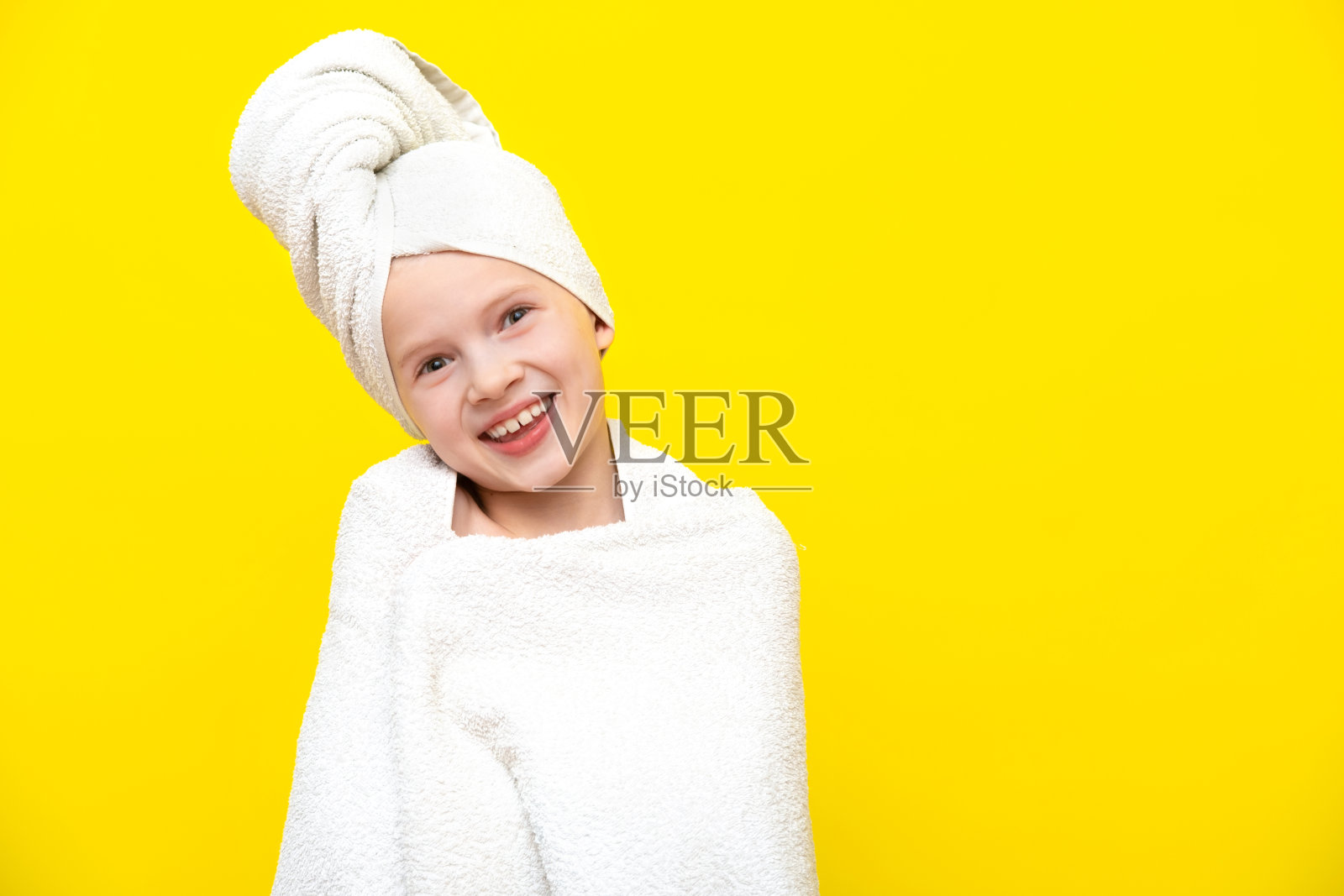 可爱的小白人女孩的肖像裹在白色毛巾与浴巾在头上在黄色工作室背景。水疗程序，沐浴纺织品照片摄影图片