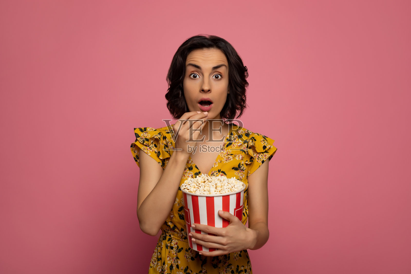 看电影。特写照片的一个年轻的惊讶女士，谁是吃爆米花和看在相机。照片摄影图片