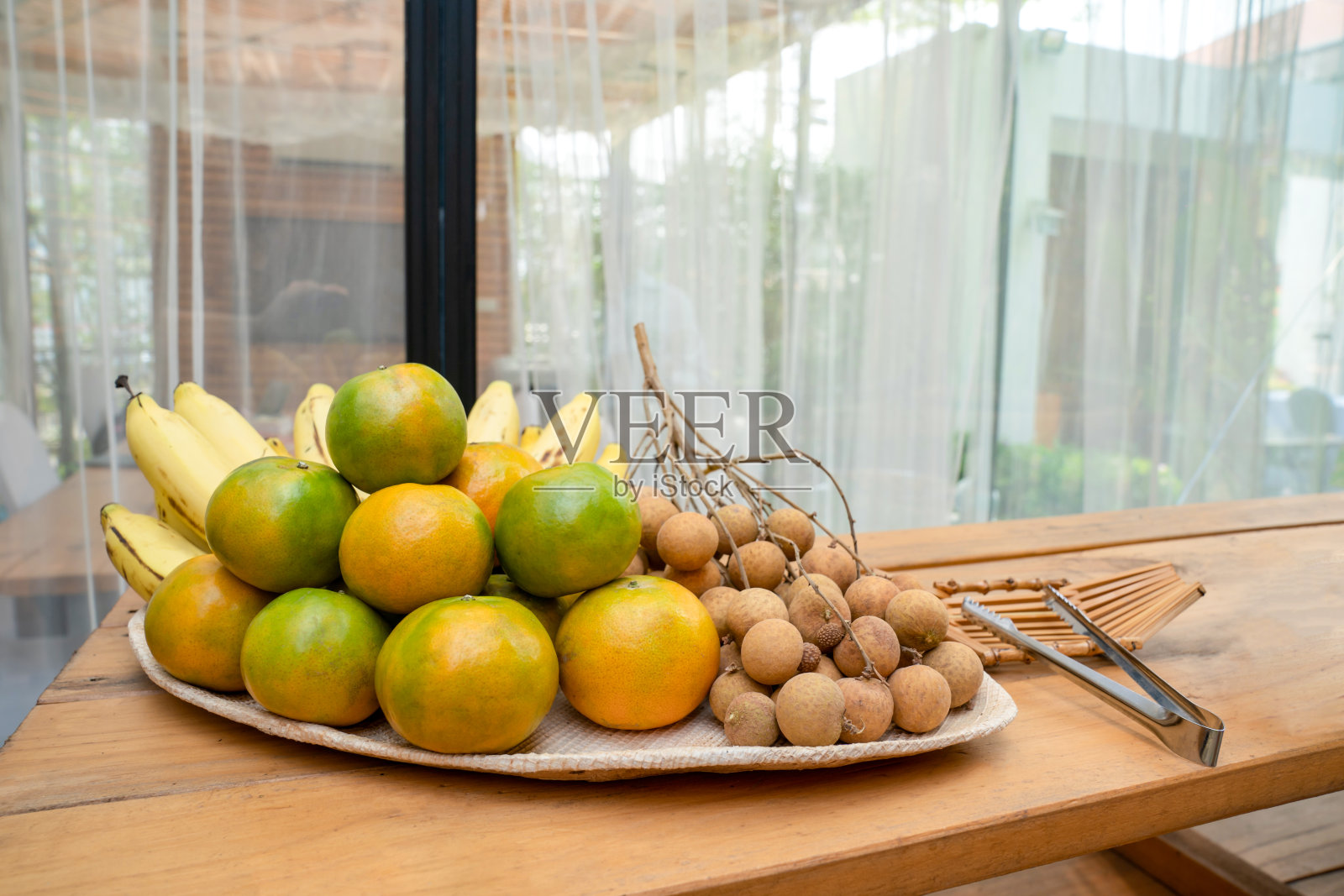 龙眼、橘子、香蕉等水果装在竹盘里摆放在户外田野的餐桌上。照片摄影图片