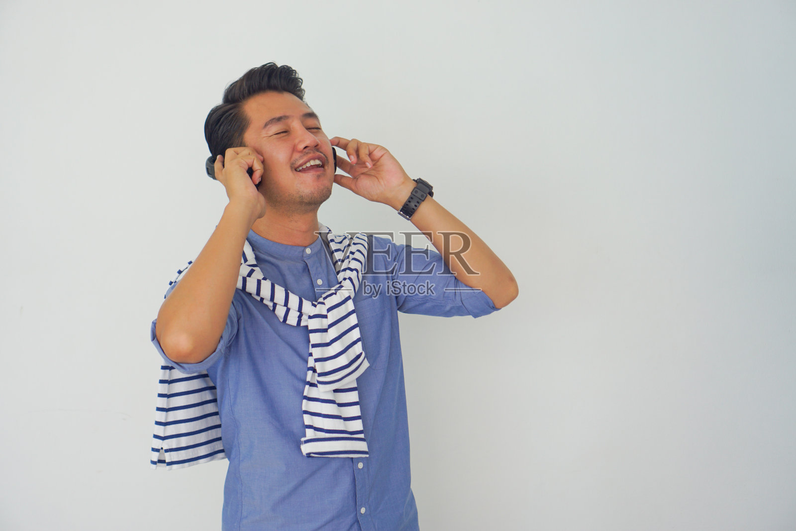 英俊的亚洲男子站在听音乐耳机和享受，微笑在白色的背景照片摄影图片