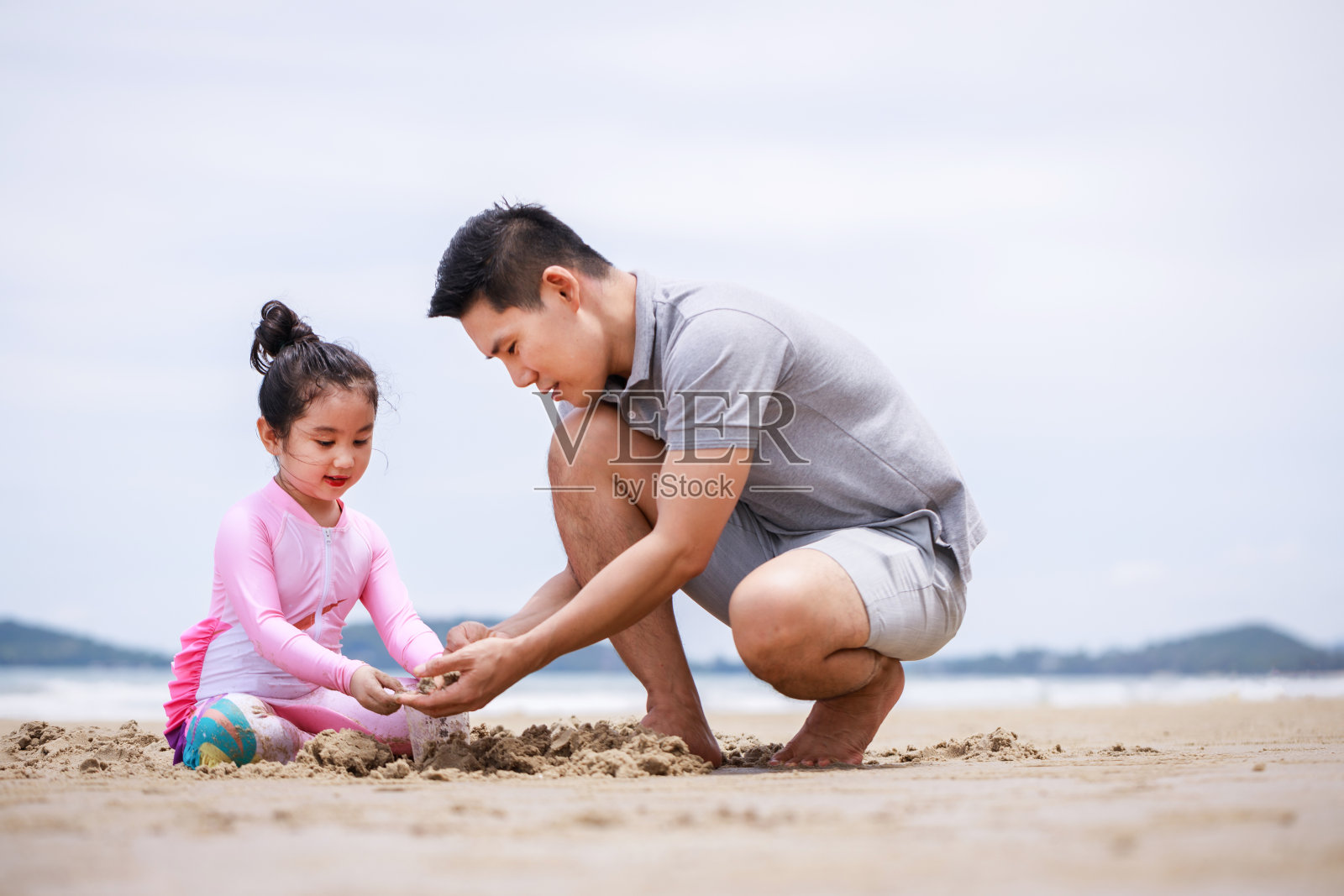 幸福的家庭。快乐假期的假期。快乐的爸爸和女儿正在热带海滩上建造沙堡，在夏天一起玩耍照片摄影图片