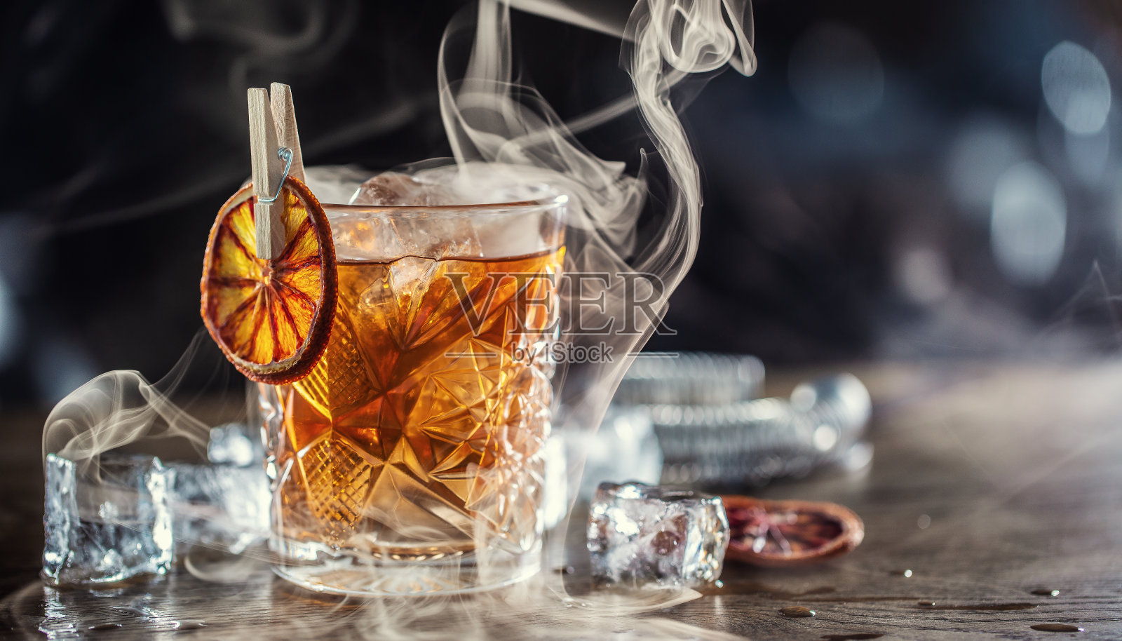 烟熏老式朗姆酒鸡尾酒与冰块周围在黑暗的背景照片摄影图片