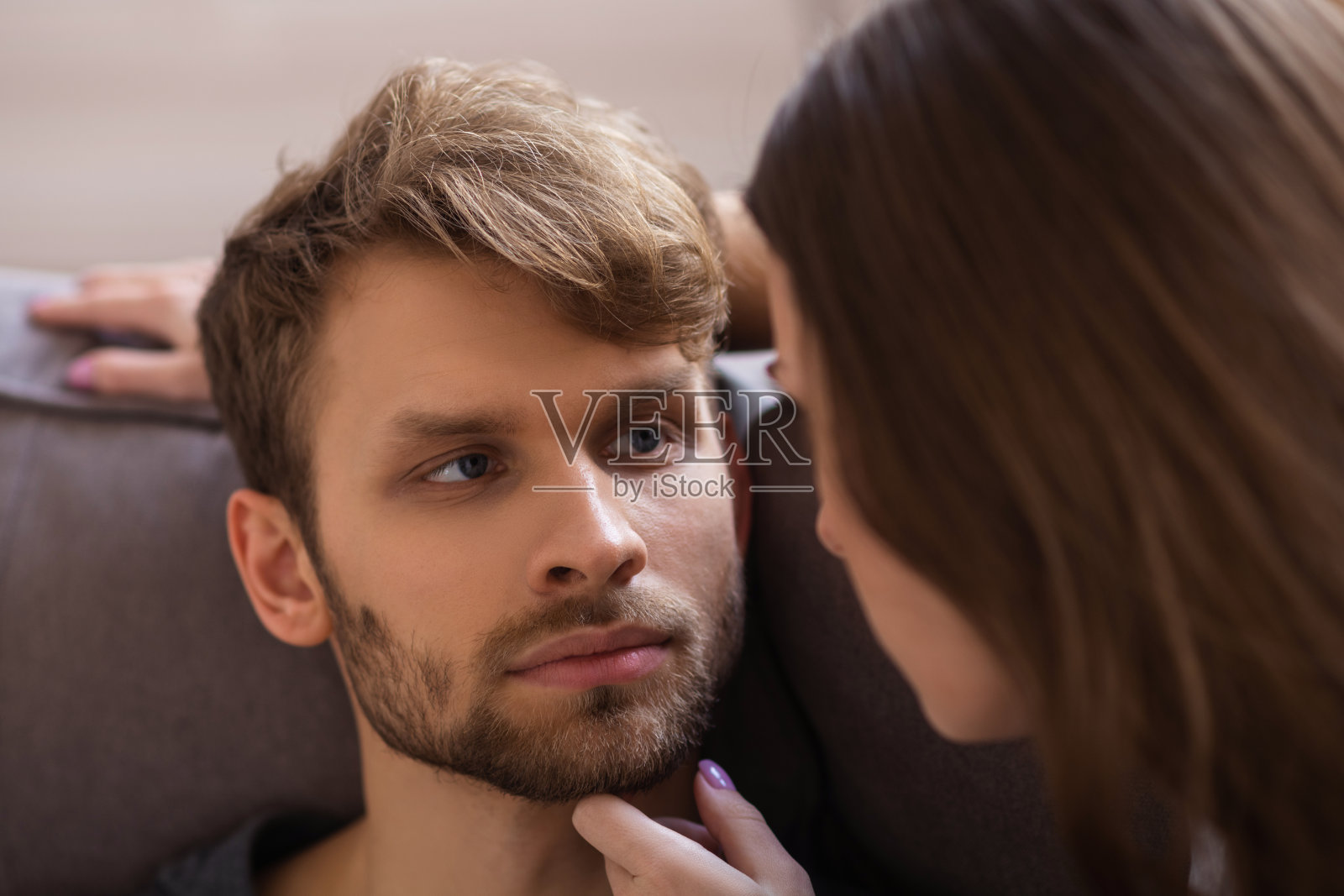 年轻的胡子英俊的男人看起来很严肃，而他的妻子触摸他的脸照片摄影图片