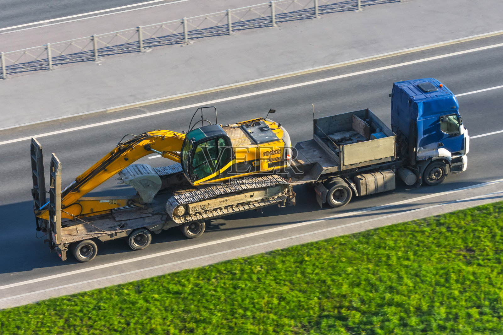 重型黄色挖掘机载着长挂车平台在市区高速公路上行驶。照片摄影图片