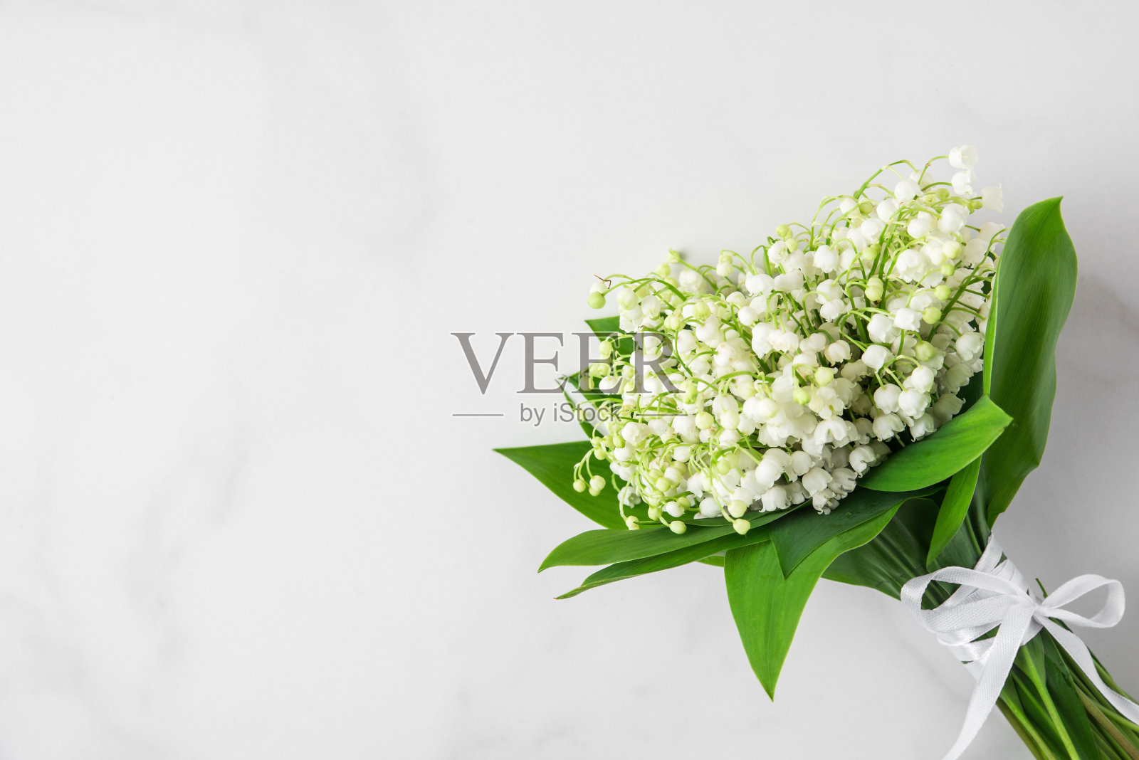 白色大理石背景上的铃兰花束。平的。顶部视图与复制空间。结婚的概念照片摄影图片
