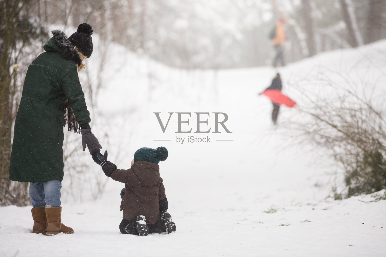 母亲和蹒跚学步的小男孩走在冬天的森林里，玩雪。家庭享受冬天。孩子和女人在外面看飘落的雪。冬天，圣诞节和生活理念。照片摄影图片