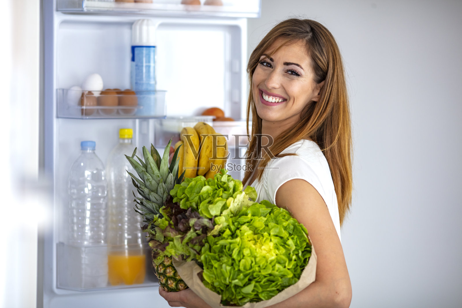 从冰箱里拿水果和蔬菜的女人。照片摄影图片