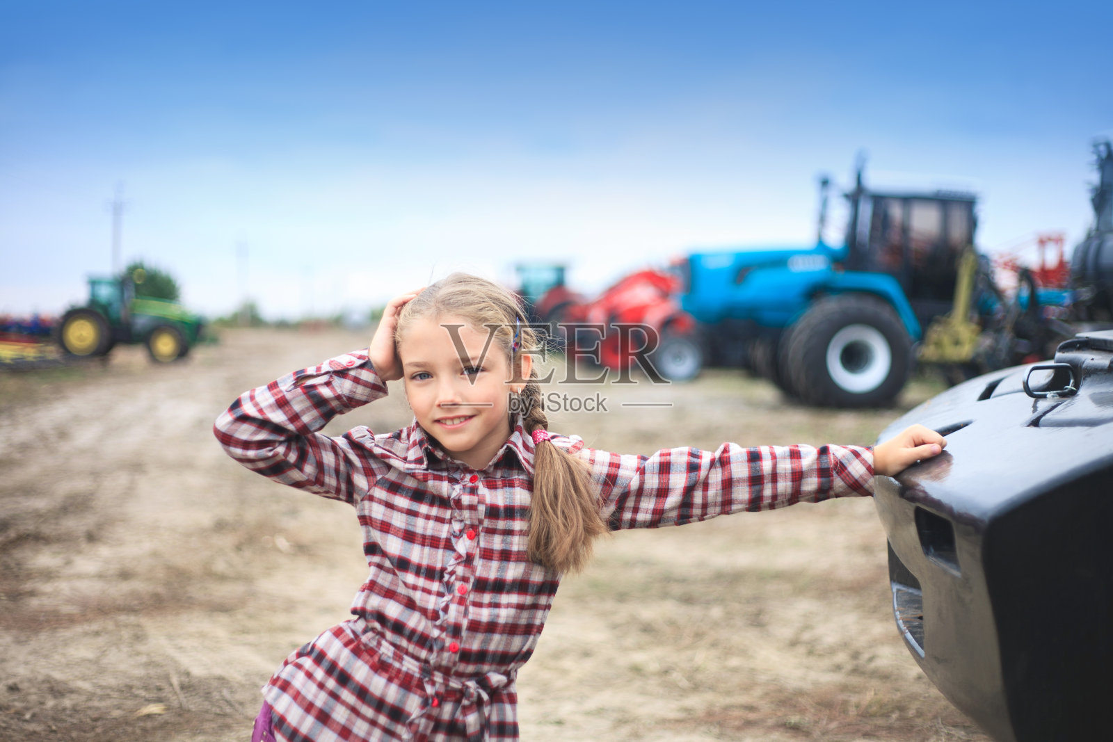 田野里现代拖拉机旁边的可爱女孩。实地工作的概念。照片摄影图片