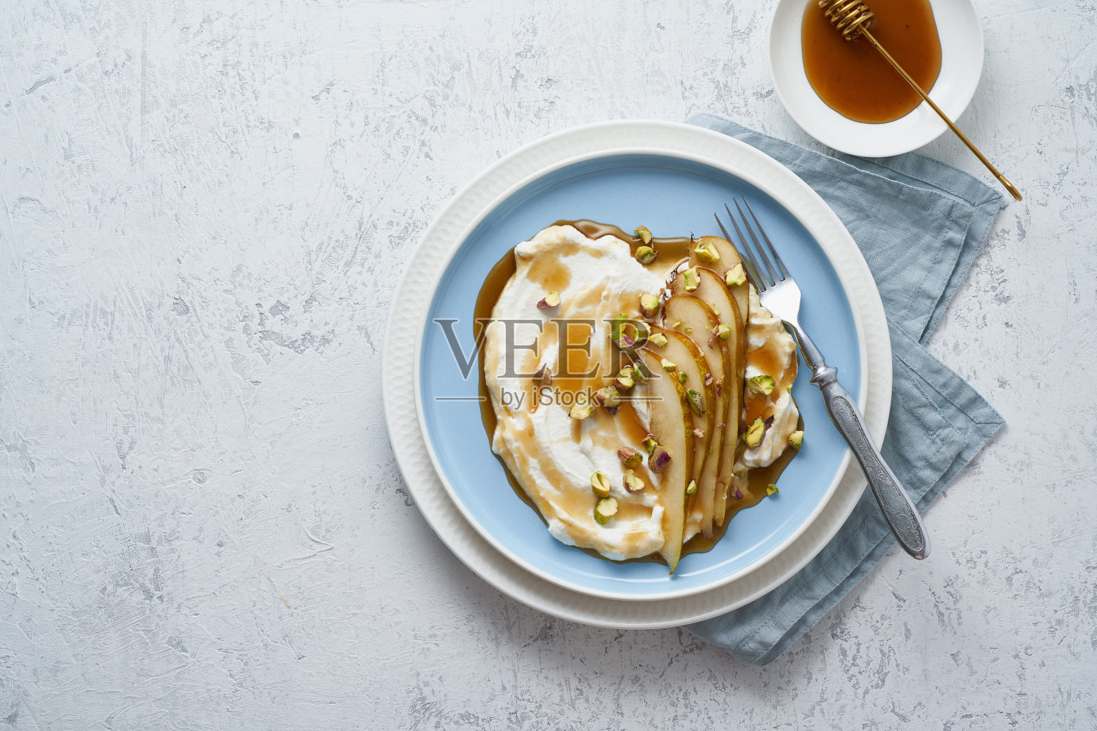乳清干酪配梨、开心果、蜂蜜或枫糖浆，放在蓝色的盘子里，放在白色的桌子上。照片摄影图片