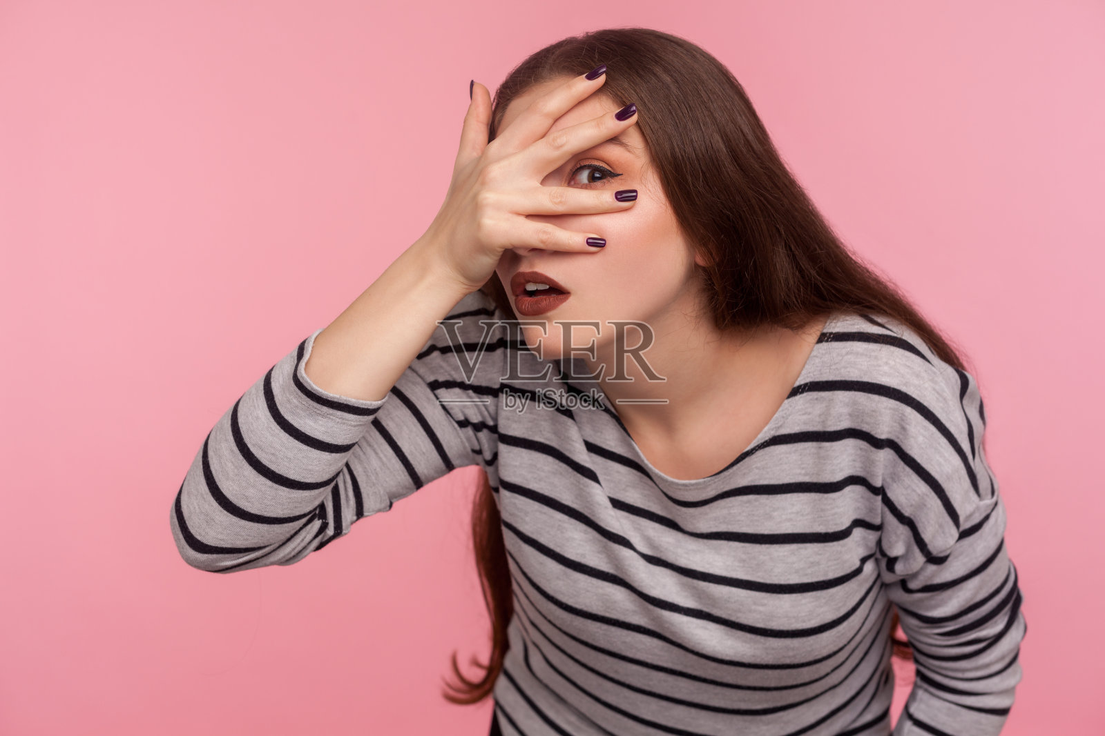多管闲事的女人的肖像在条纹运动衫看通过手指好奇和可疑的表情照片摄影图片