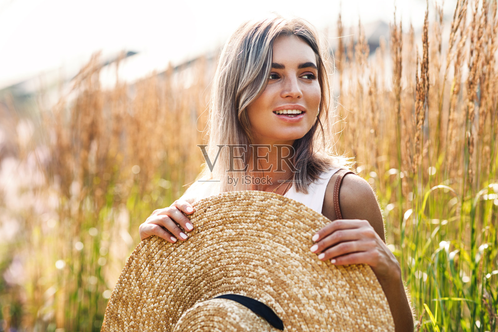 一个年轻漂亮的女人，手里拿着一顶大草帽，站在被高草环绕的田野上照片摄影图片