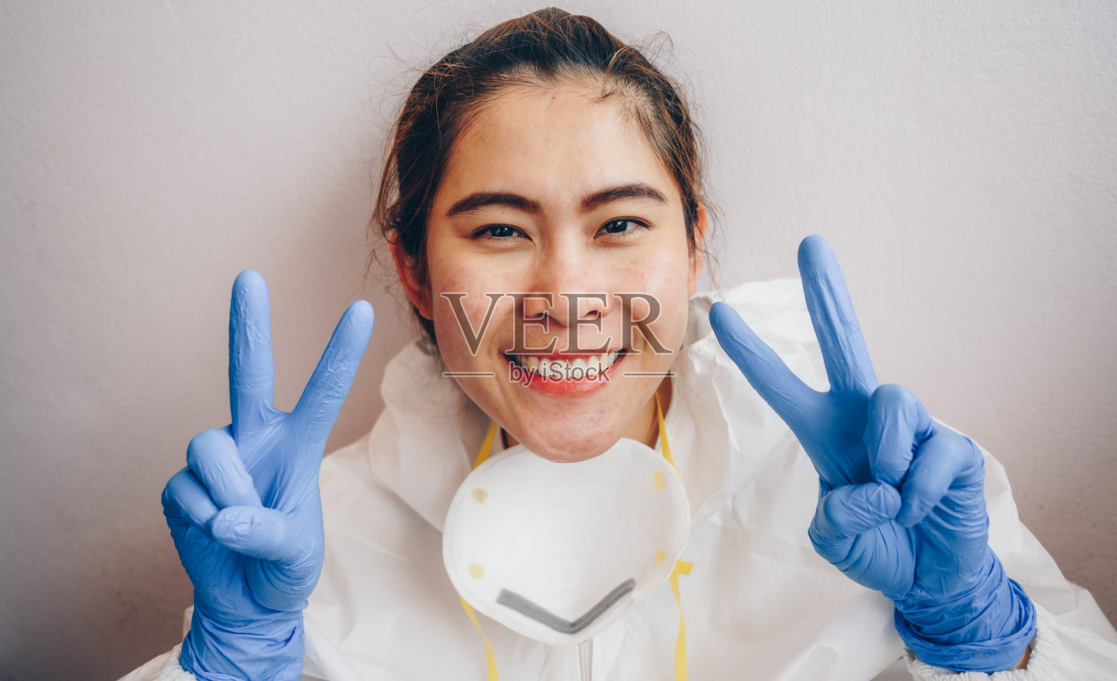 covid-19大流行期间，长期住院的医护人员在下班后戴医用口罩，脸上有伤口和痤疮，但仍面带微笑，露出胜利的迹象。照片摄影图片