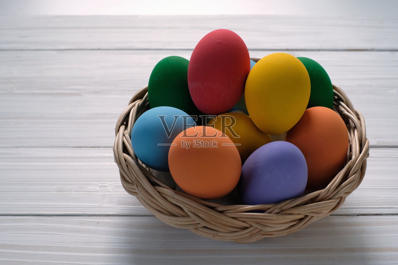 白色木制背景的篮子里装着五颜六色的鸡蛋照片摄影图片