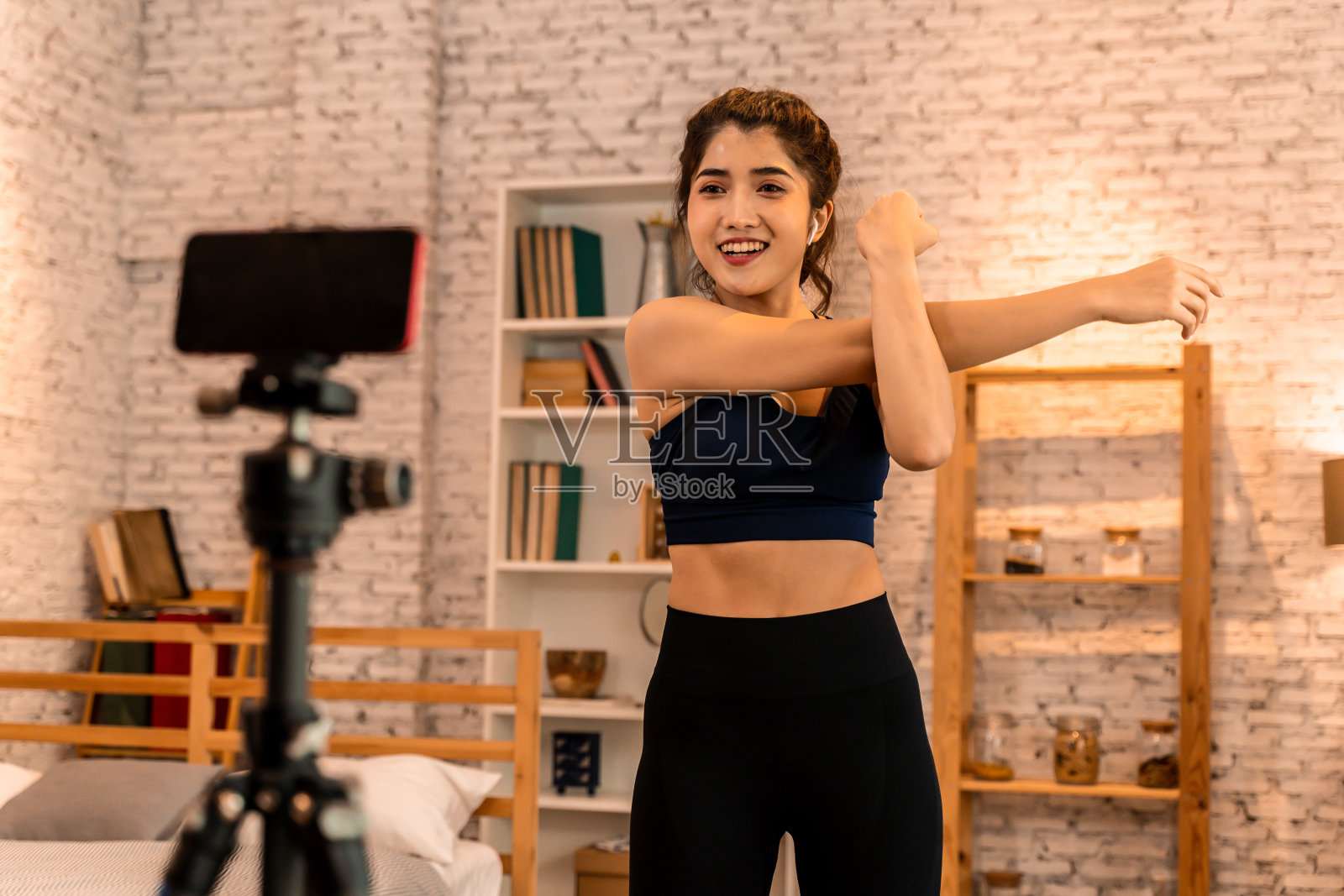 20多岁的年轻亚洲女性穿着运动服对着镜头说话，并在网上解释健身教程。健康女孩博客在家里的客厅。教授网上健身课的概念照片摄影图片