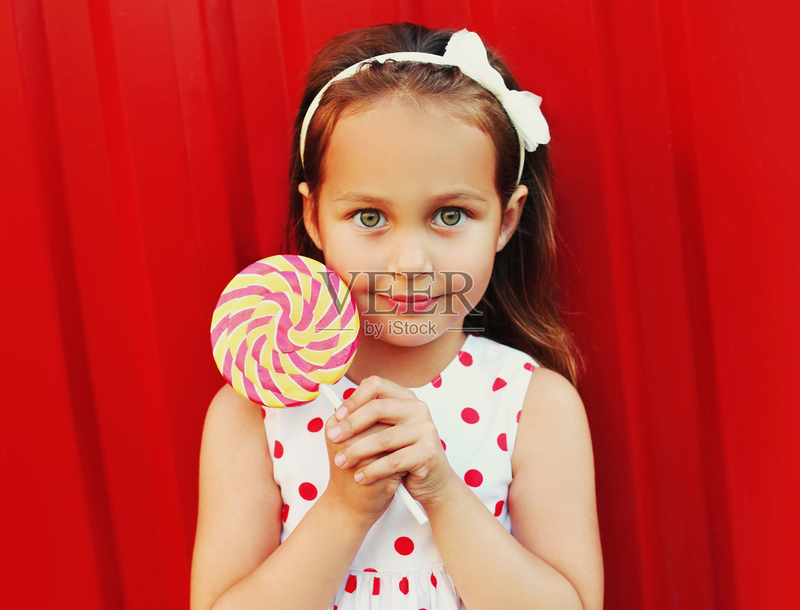 可爱的小女孩的肖像与棒棒糖穿着裙子在红色的背景照片摄影图片