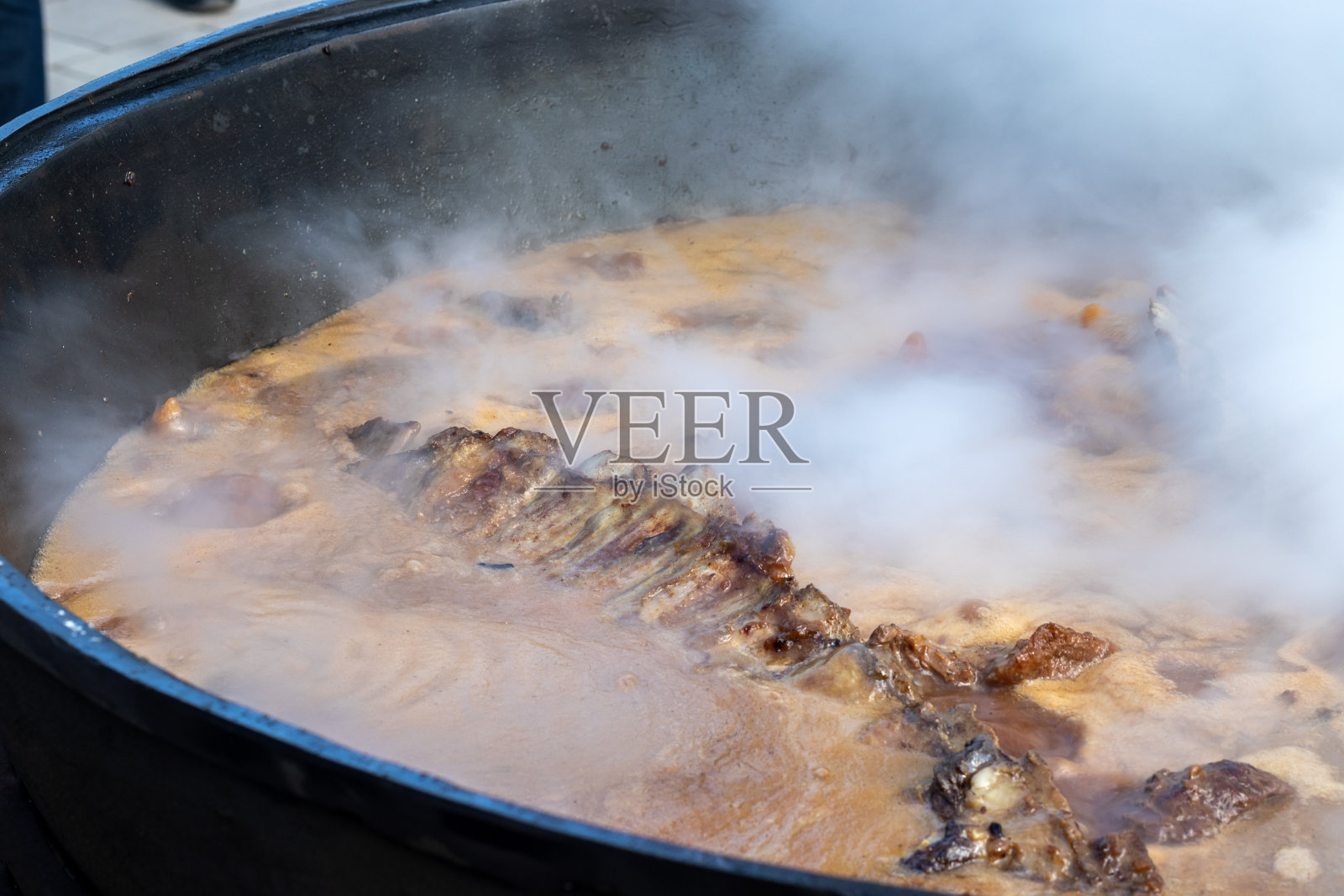 做真正的乌兹别克肉饭。在一个传统的民间节日里，在一个充满蒸汽的大锅里炖羊排照片摄影图片